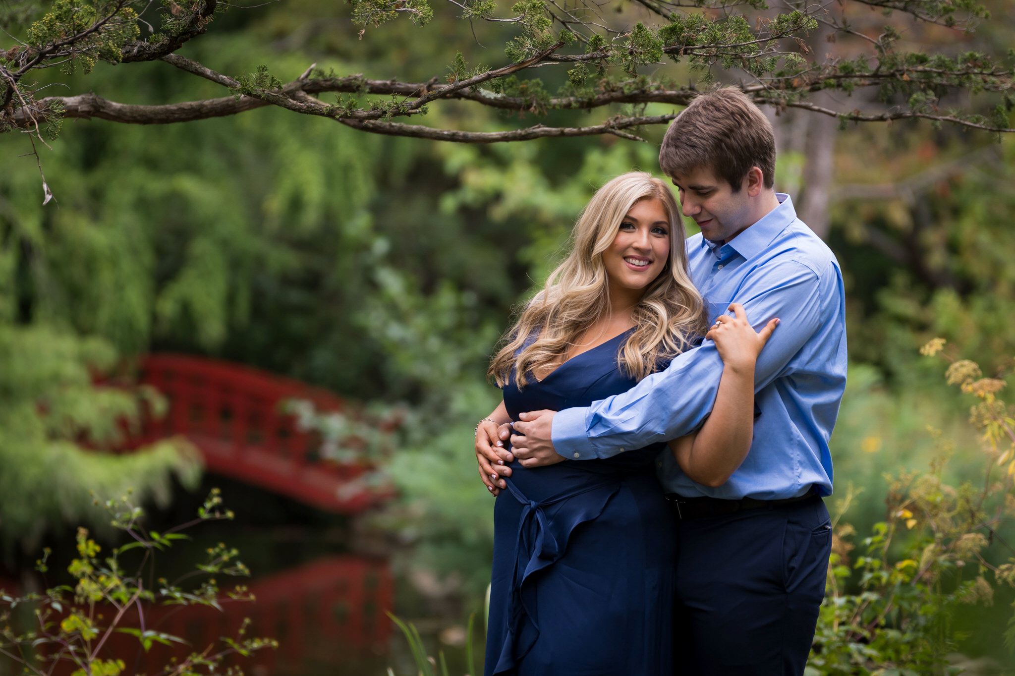 A couple hug with a red bridge in the background during their Cranbrook engagement session.  