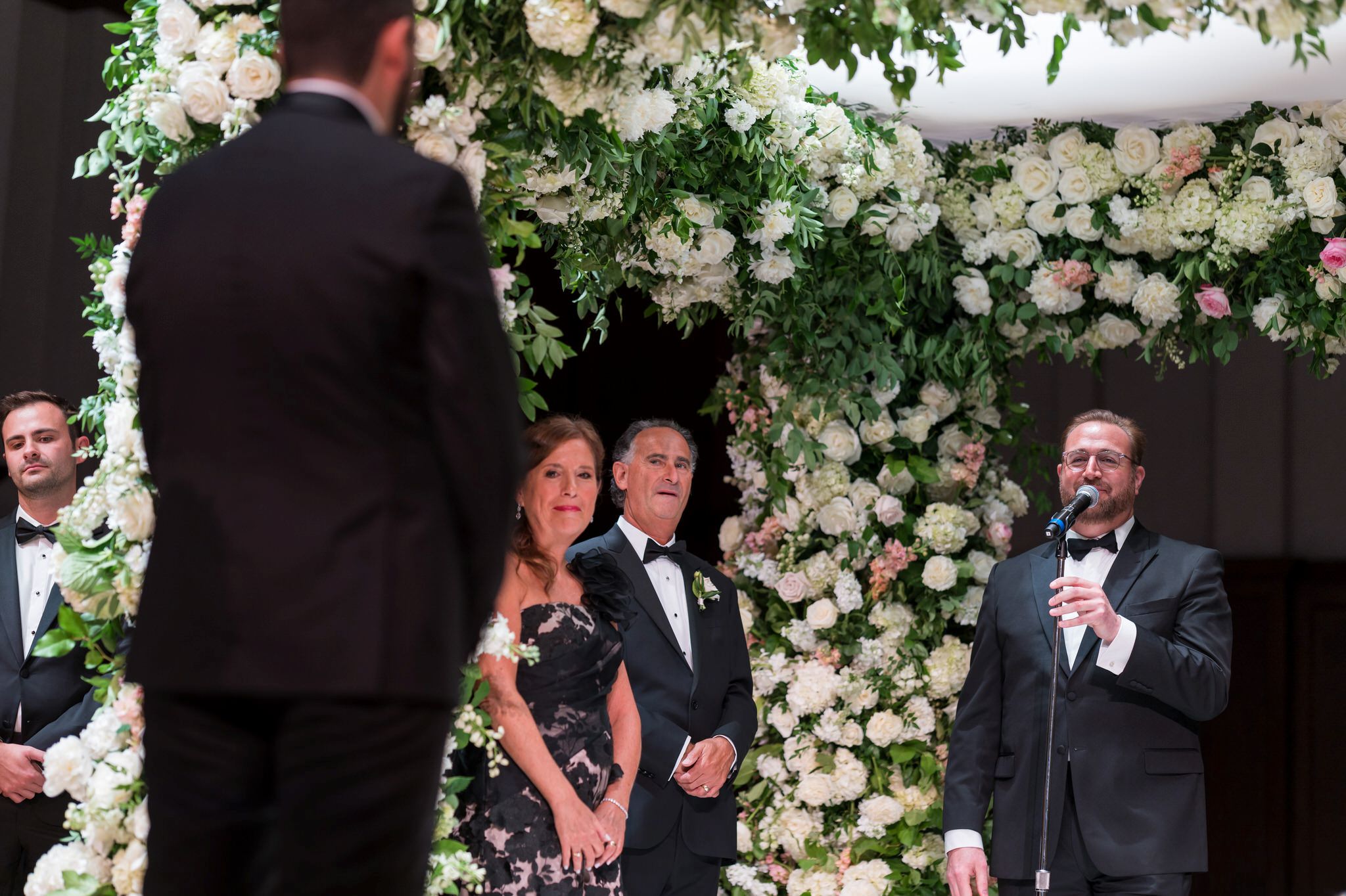 A jewish cantor sings under a floral chuppah.  
