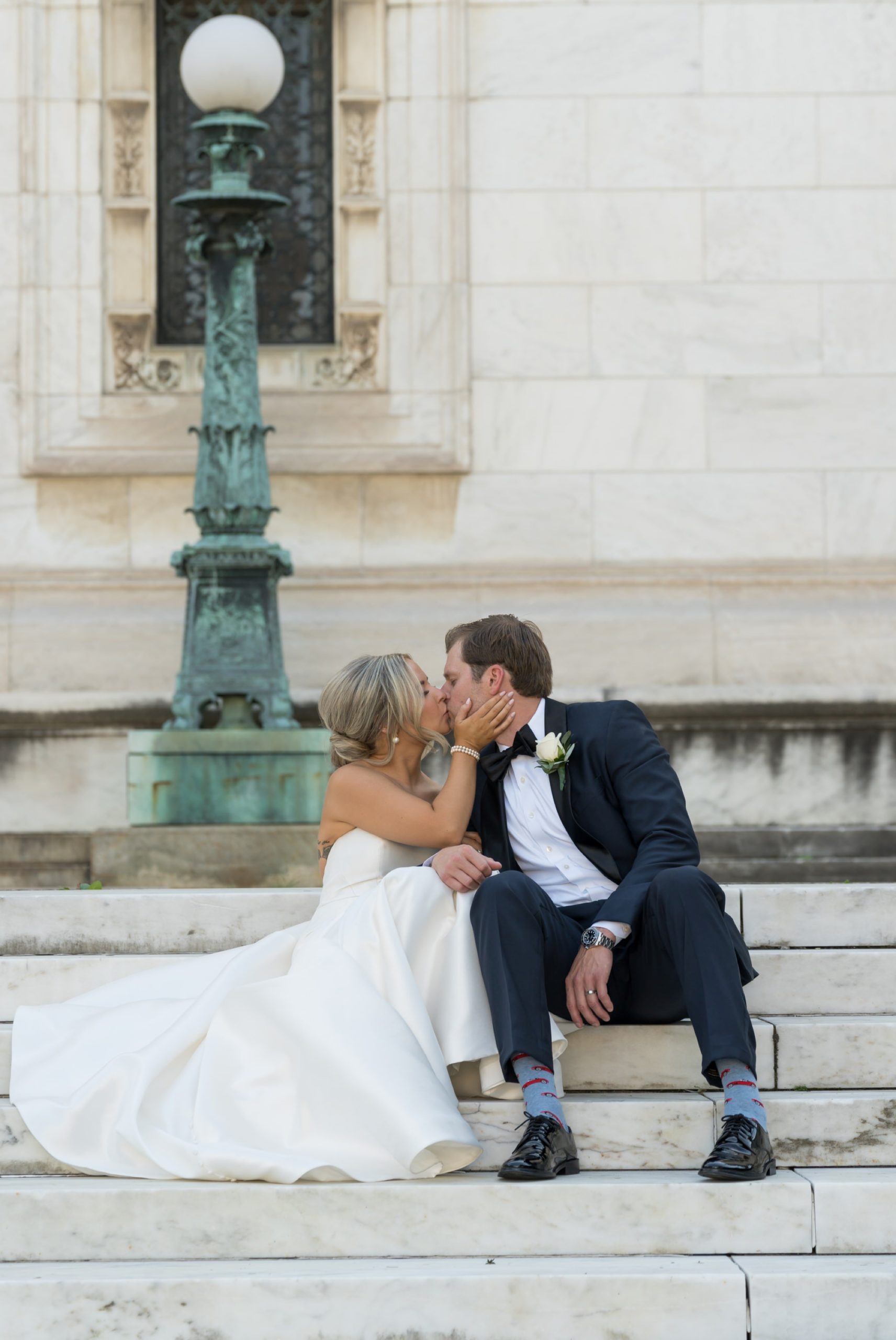 Bride and groom sit on marble steps outside of the Detroit Public Library and kiss. 