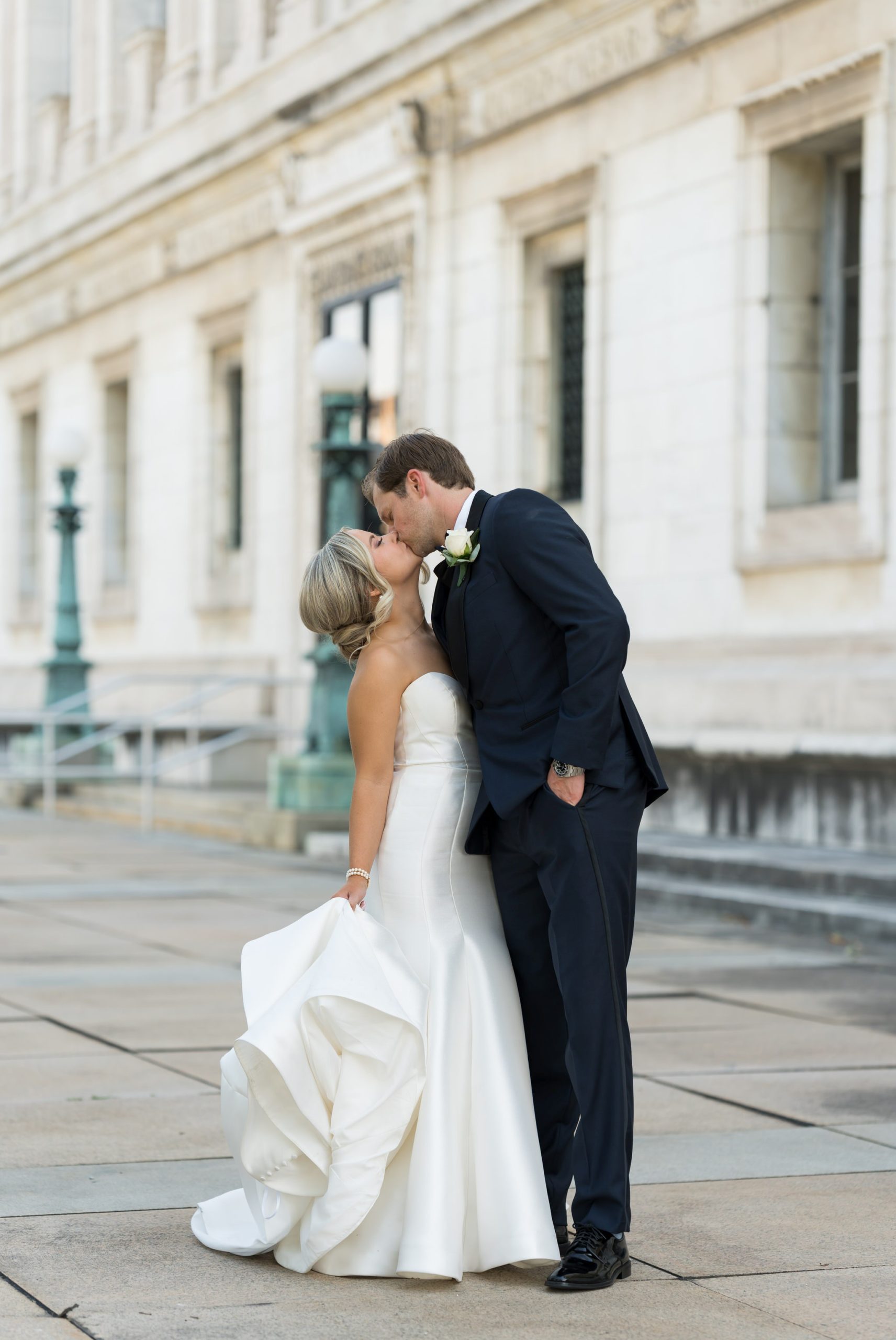 A bride, holding her dress, is kissed by her husband outside of the Detroit Public Library on their wedding day.  