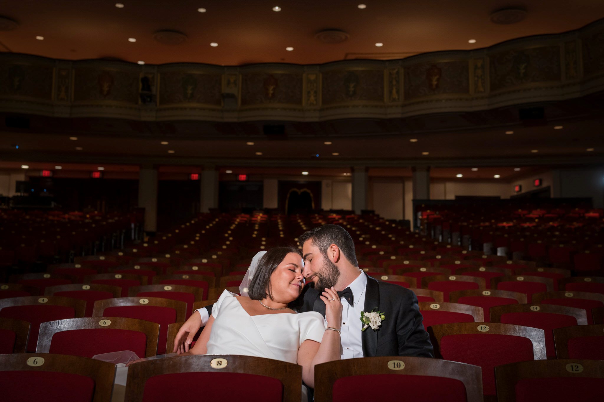 A bride and groom snuggle in the red seats of the Detroit Orchestra Hall wedding.