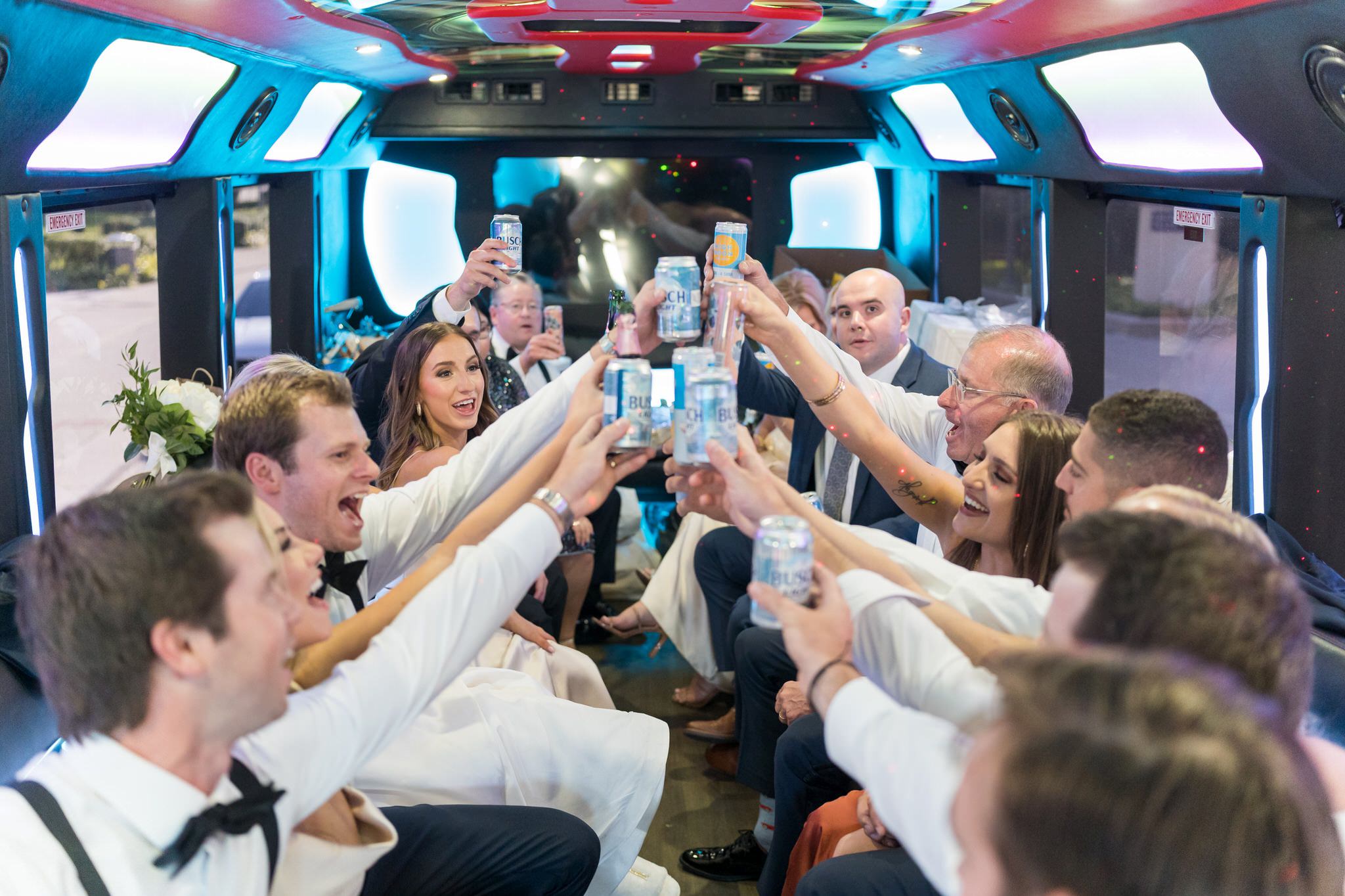 Guests hold Busch Light beer cans and toast in a party bus.