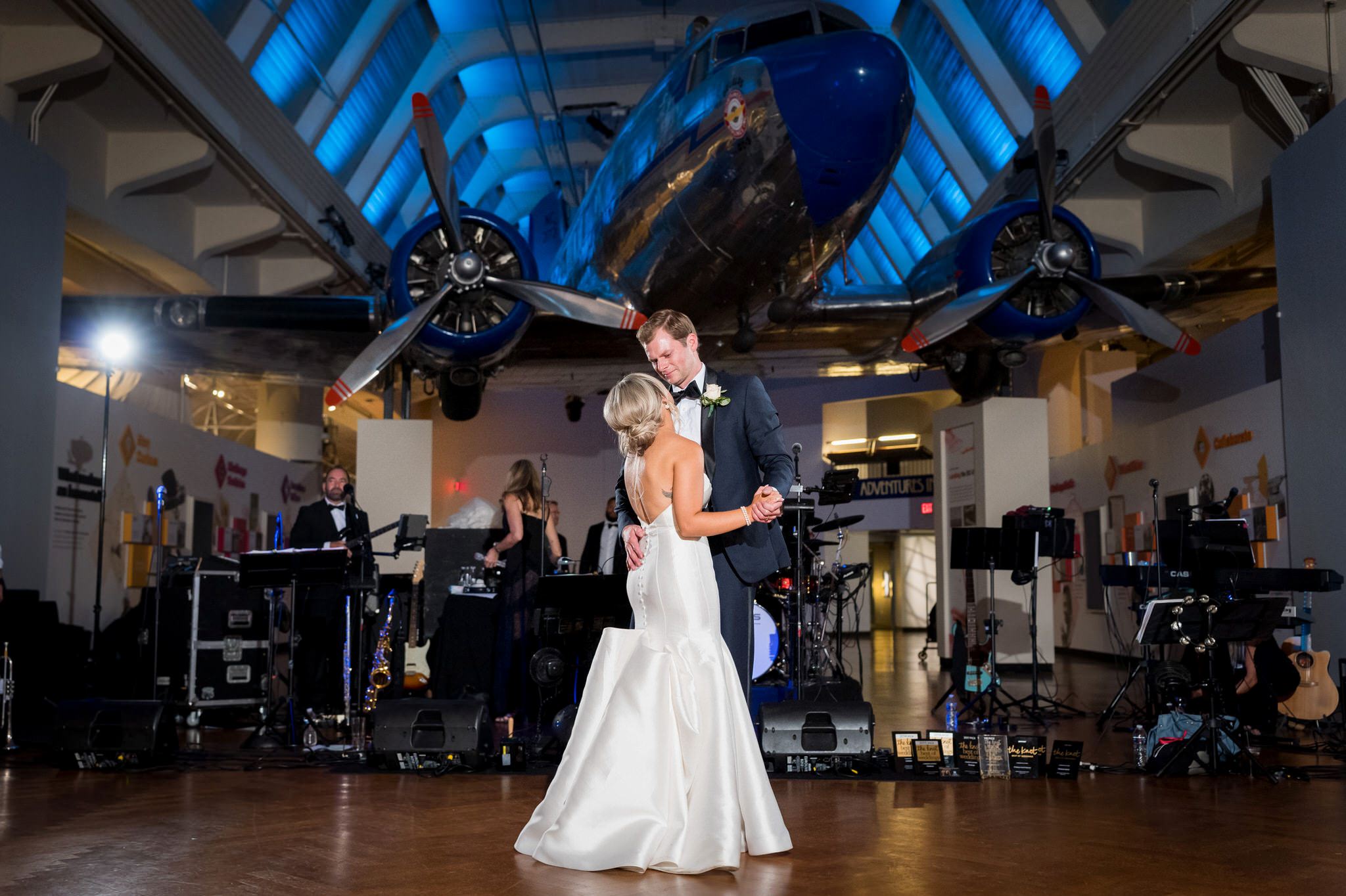 A bride and groom dance in front of a suspended airplane at a Henry Ford Museum wedding. 
