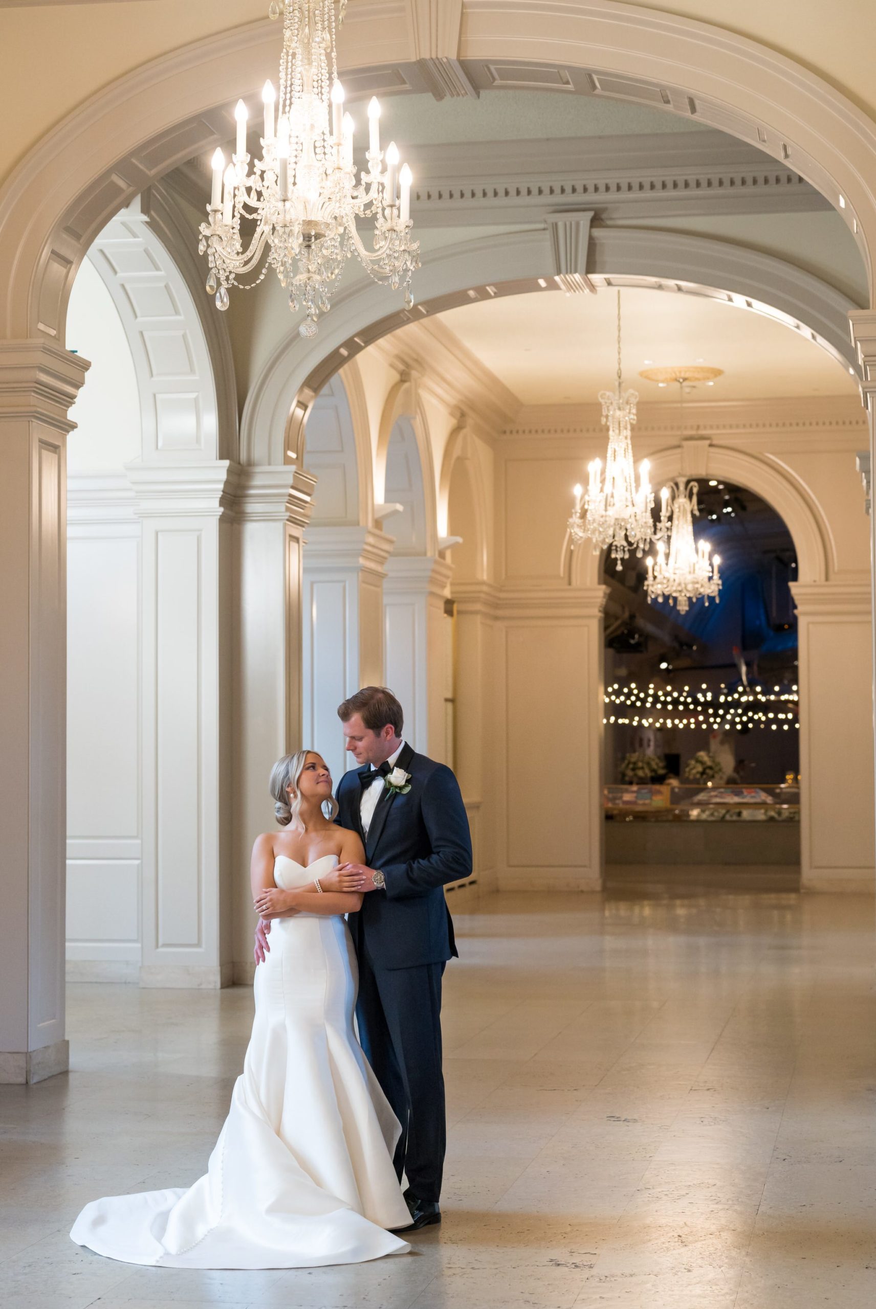 A bride and groom pose, holding each other, in the hallway of their Henry Ford Museum wedding. 