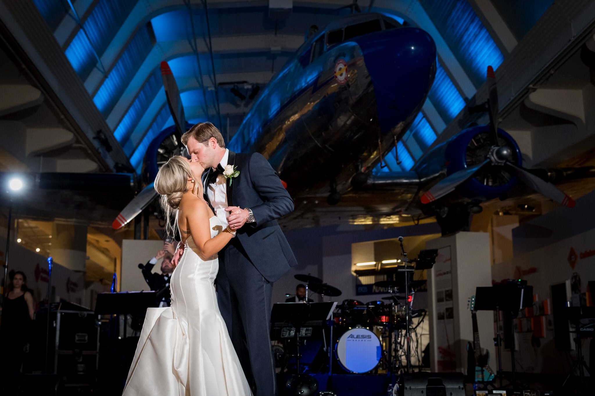 A bride and groom kiss with an airplane in the background at their Henry Ford Museum wedding. 