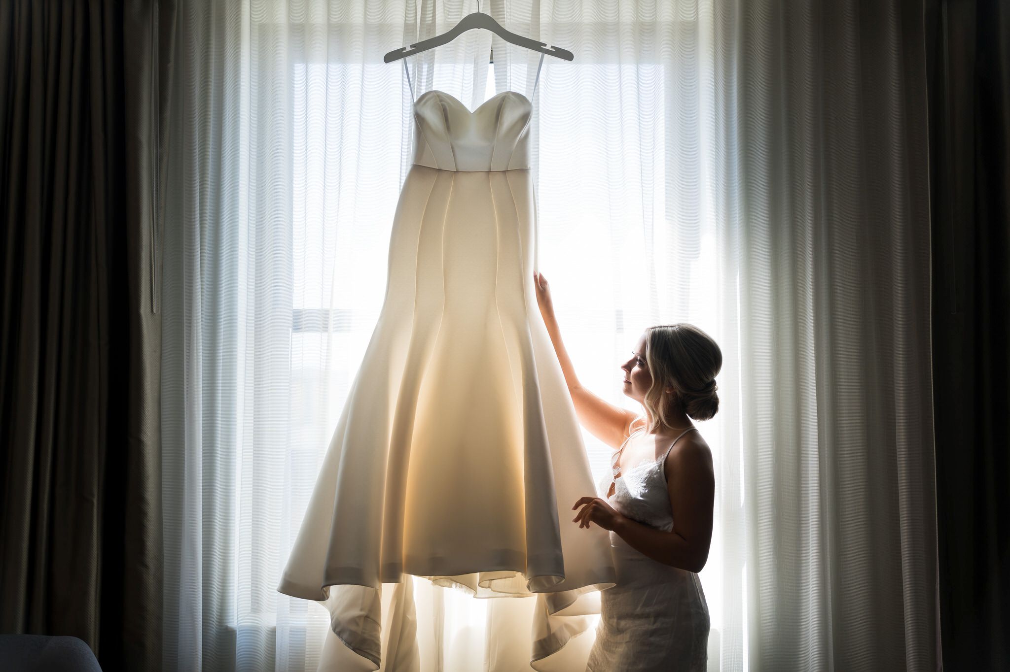 A bride looks at her wedding dress in a window by Brian Weitzel Photography.  