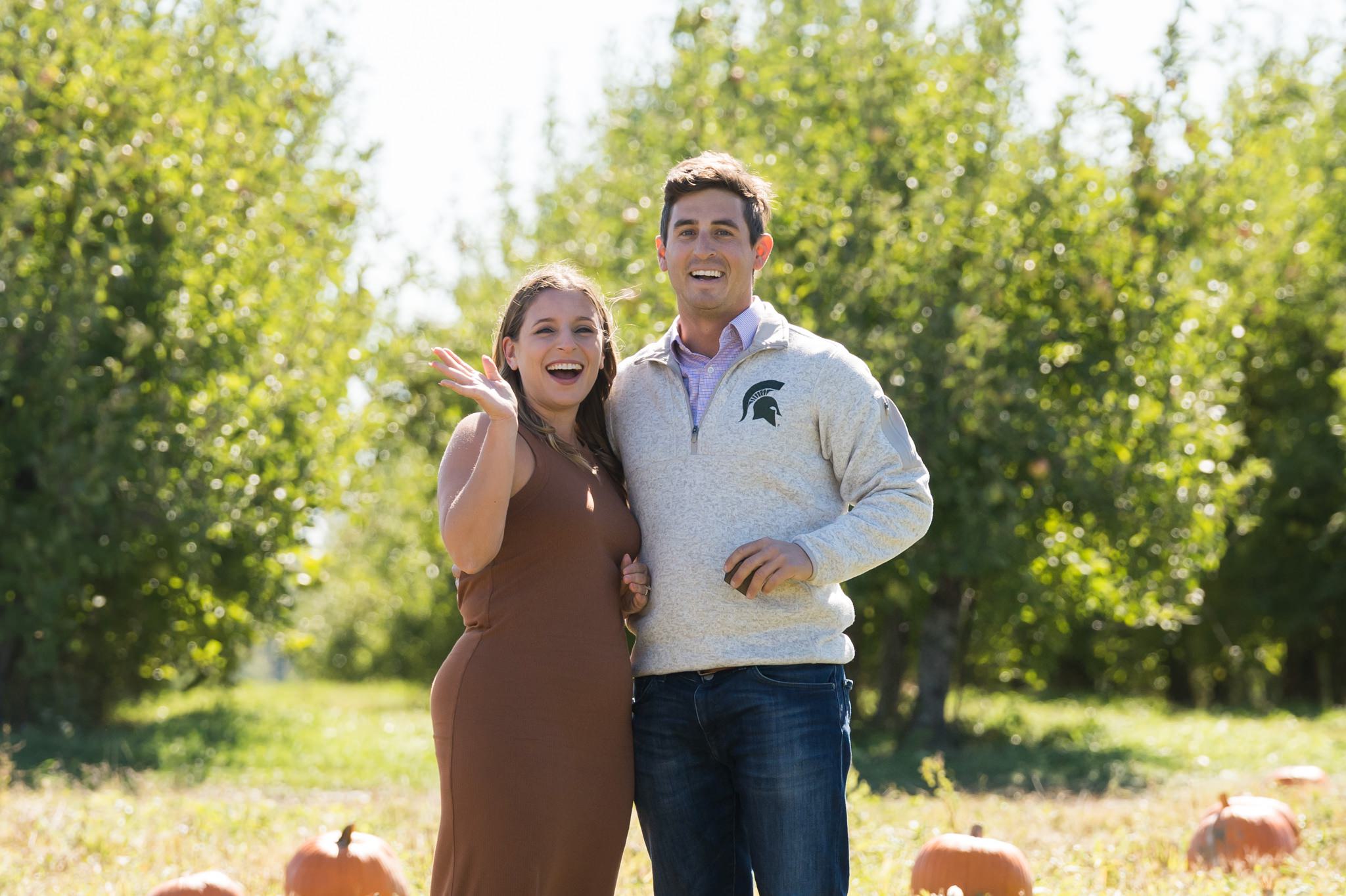 A newly engaged fiance waves at the cameras at a pumpkin patch proposal at Blake's Apple Orchard
