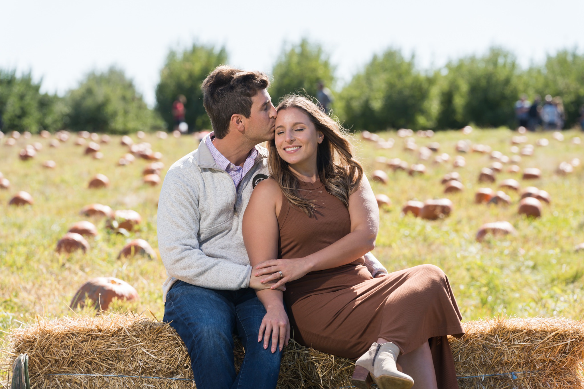 A newly engaged couple smile and kiss at their pumpkin patch proposal. 