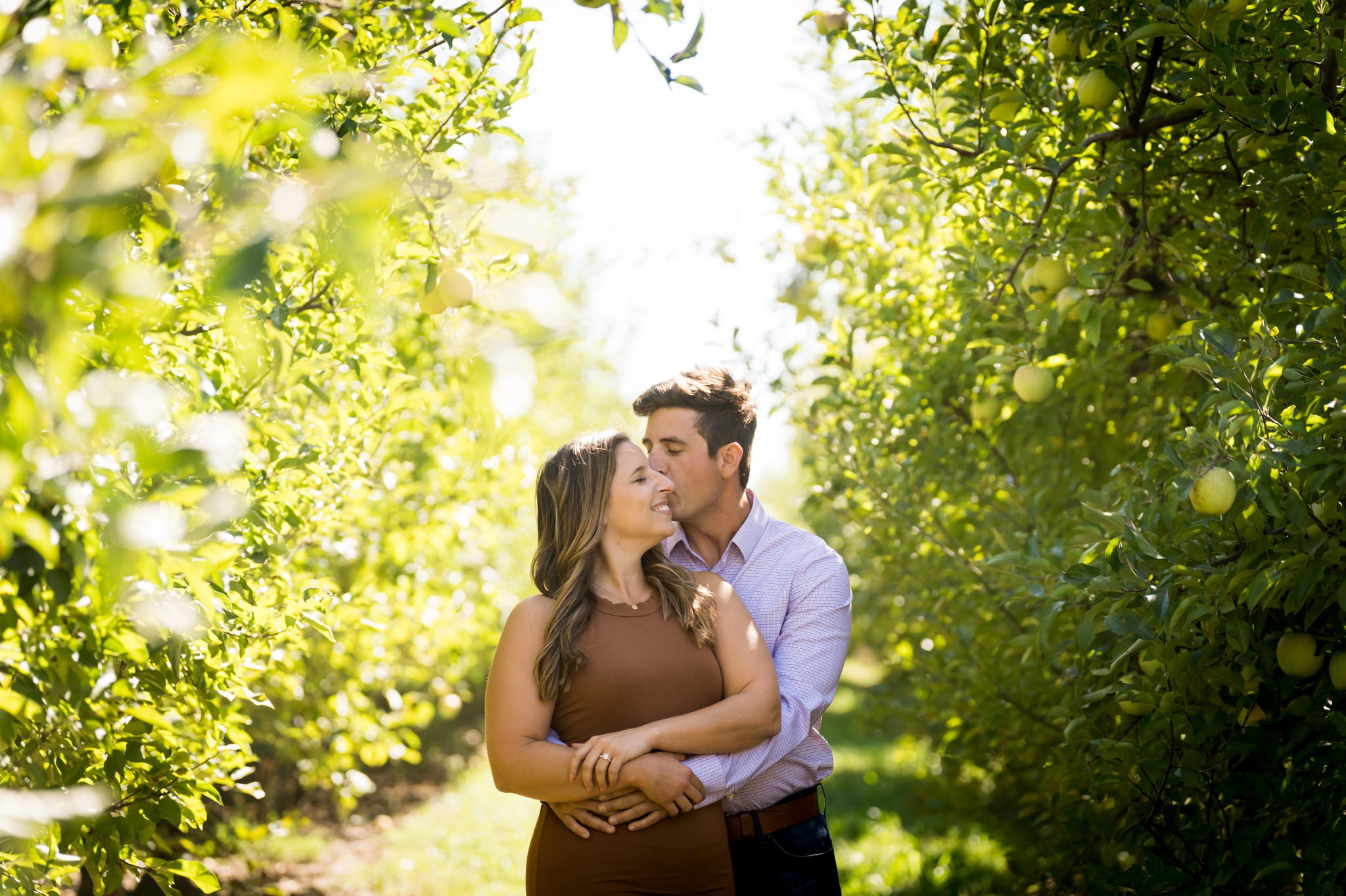 Standing in rows of apple trees, a couple embraces during their Blake's Apple Orchard engagement session.