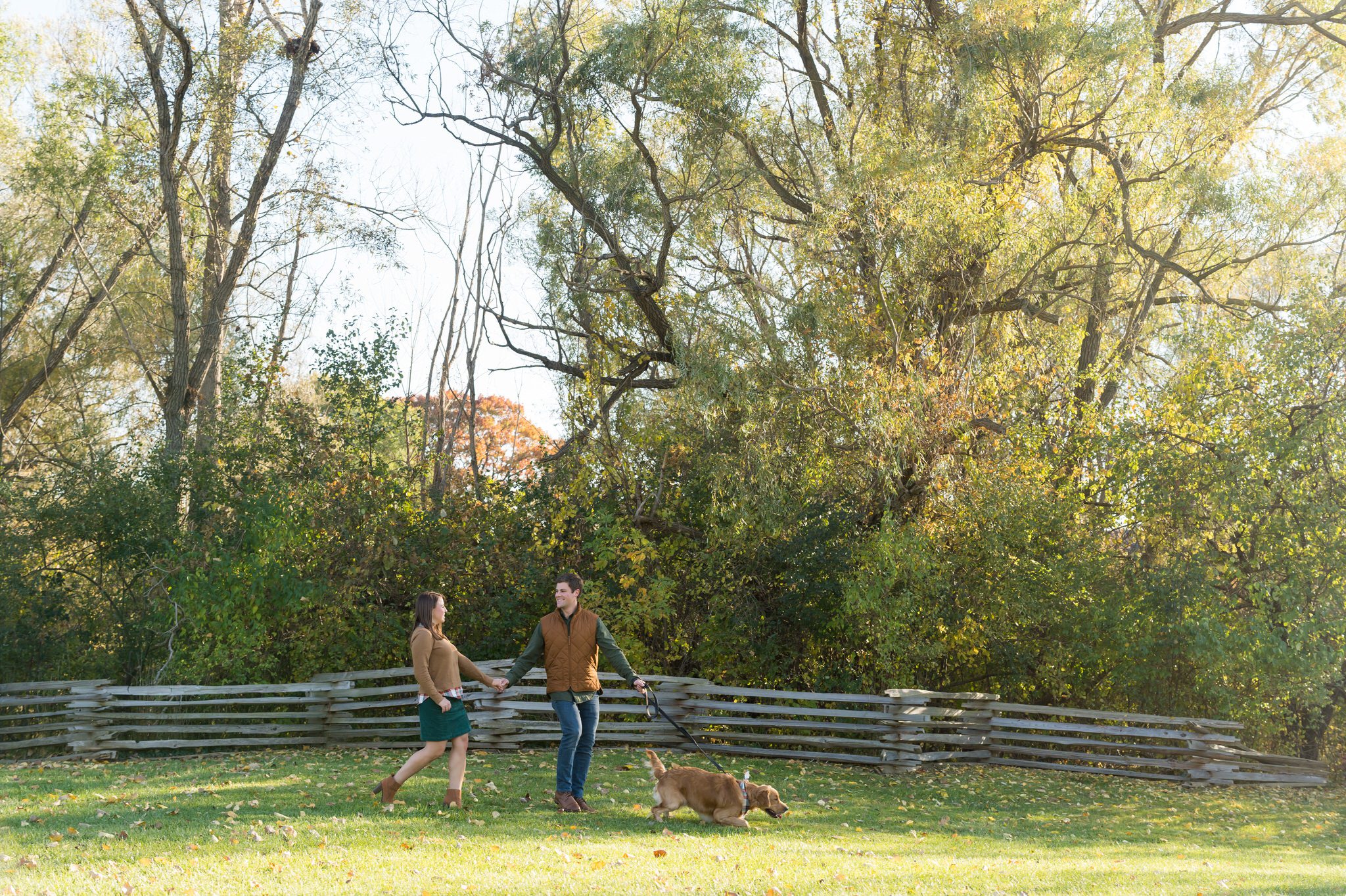 A couple walks their dog at a fall engagement at Van Hoosen. 
