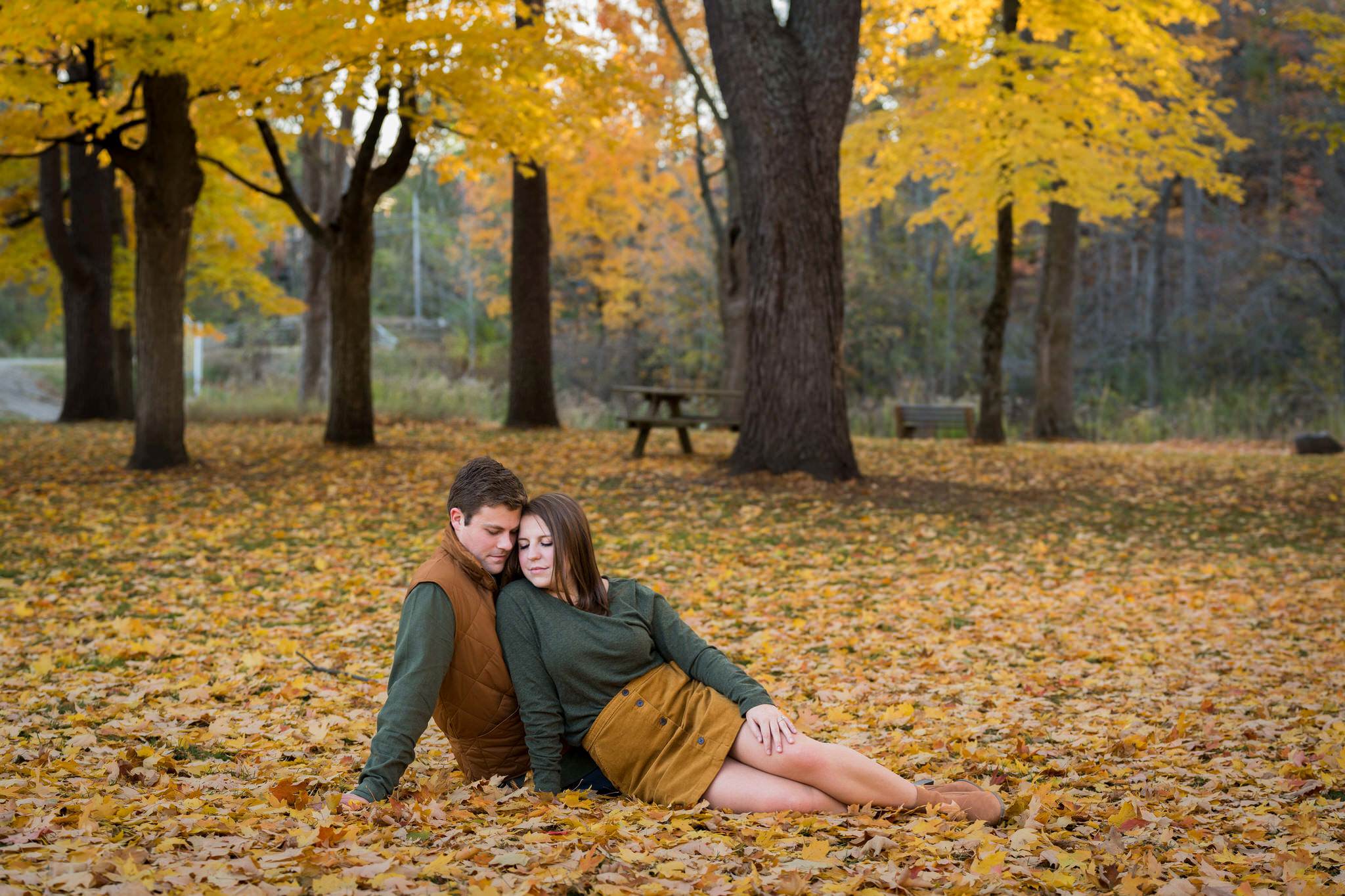 A couple sits on the ground and embraces at a fall engagement at Van Hoosen. 