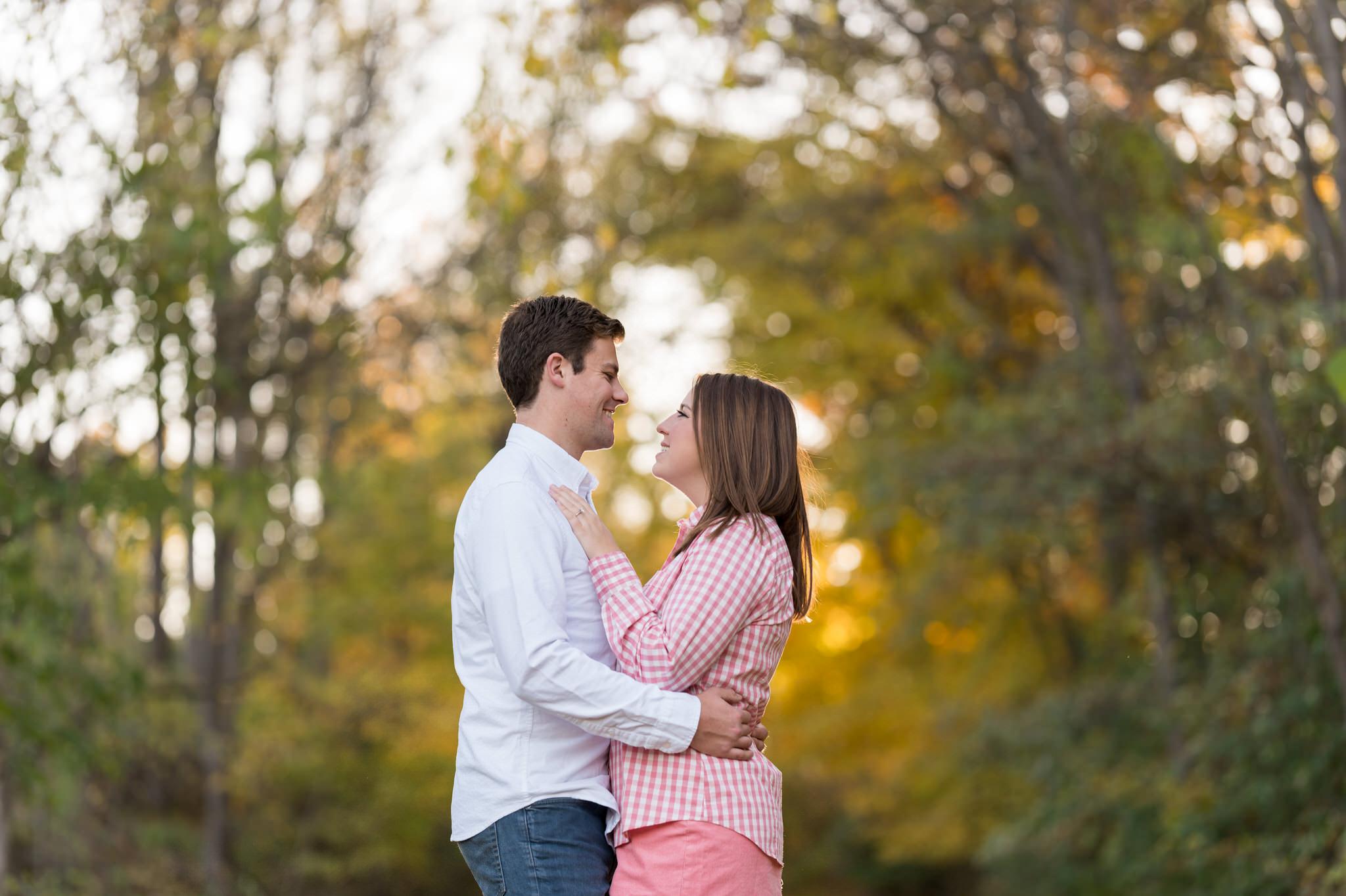 A couple hugs with the sun and trees behind them at their fall engagement at Van Hoosen. 