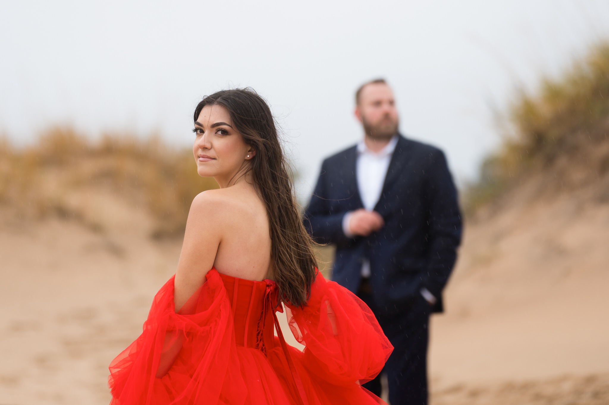 A woman, wearing a red flowing dress, looks over her shoulder at Sleeping Bear Dunes engagement session. 