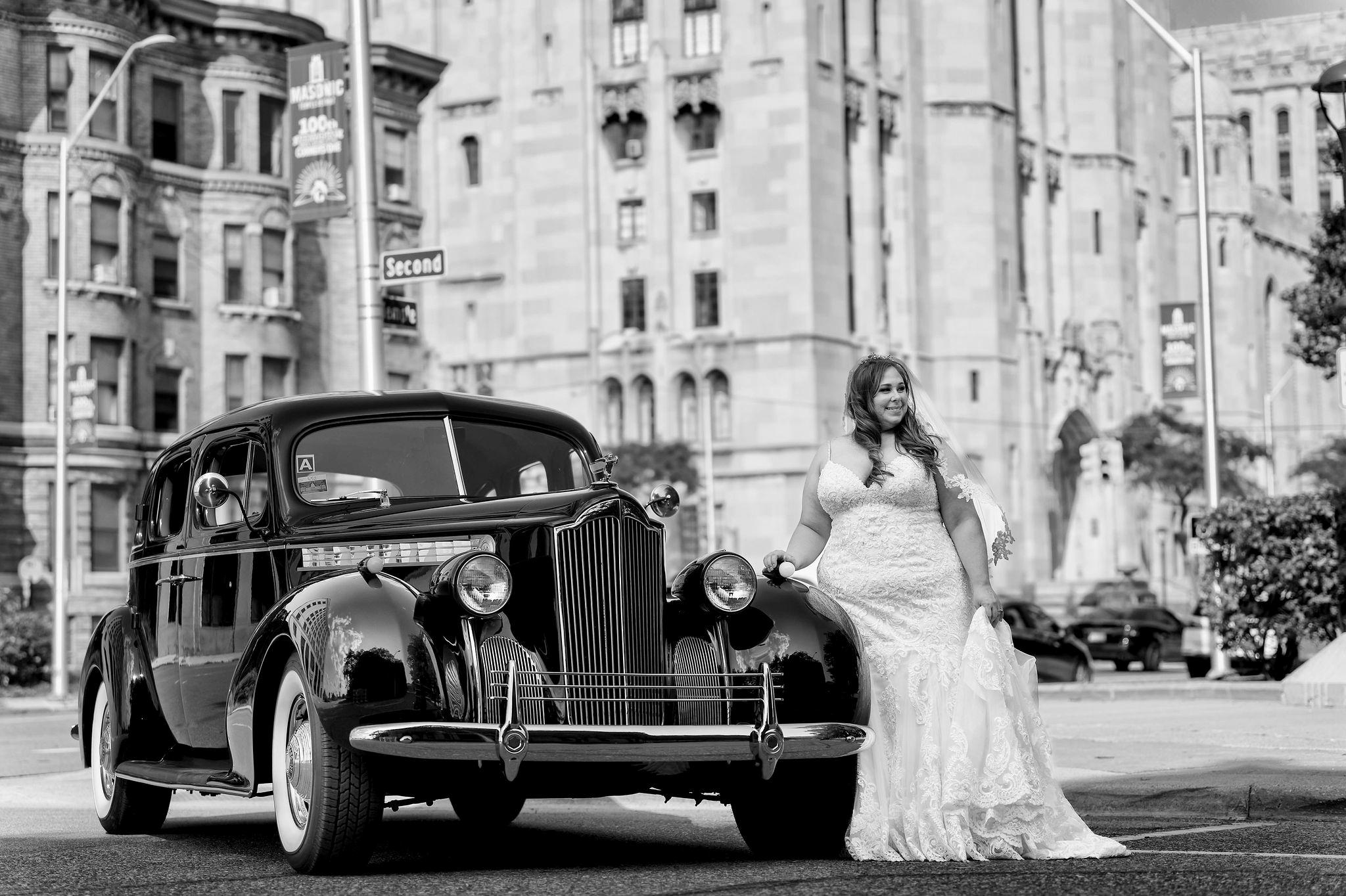 A bride poses with a classic car on the streets of Detroit near the Masonic Temple.