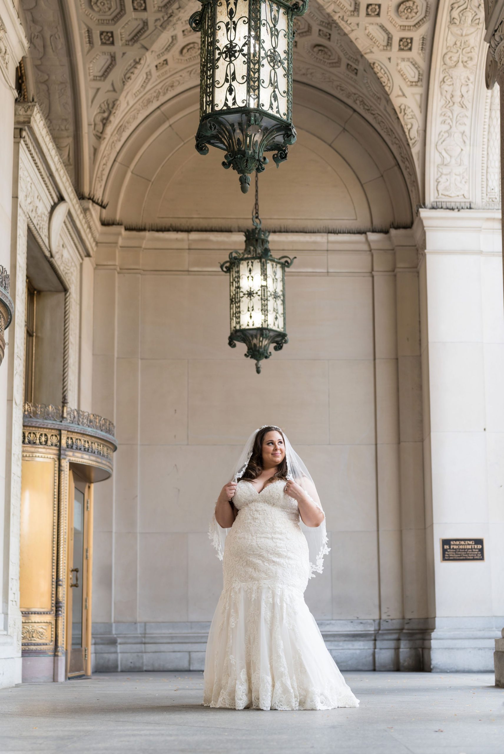 A bride poses in front of Cadillac Place Apartments in Detroit while holding her veil.