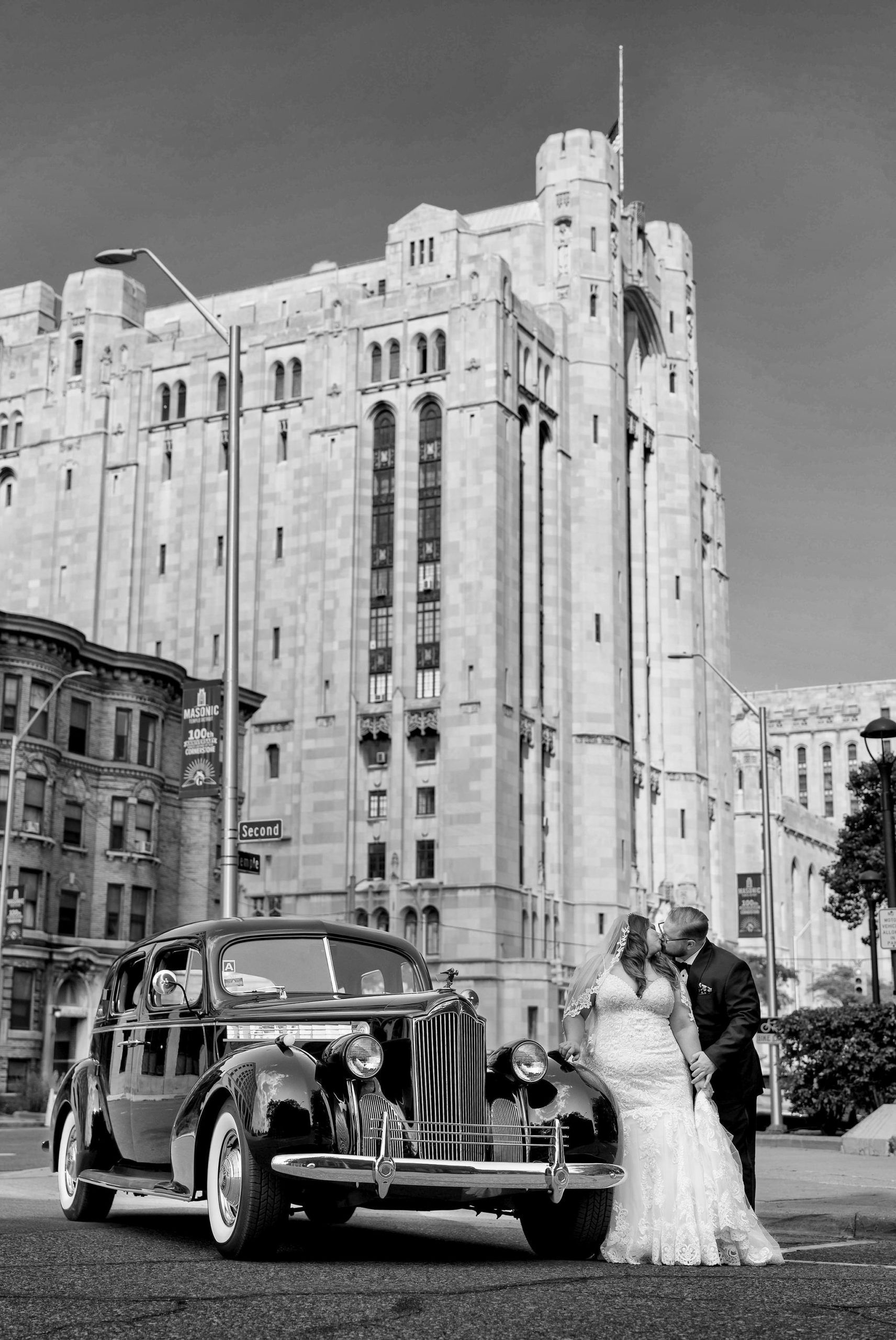 A couple poses with a classic car on the streets of Detroit near the Masonic Temple.