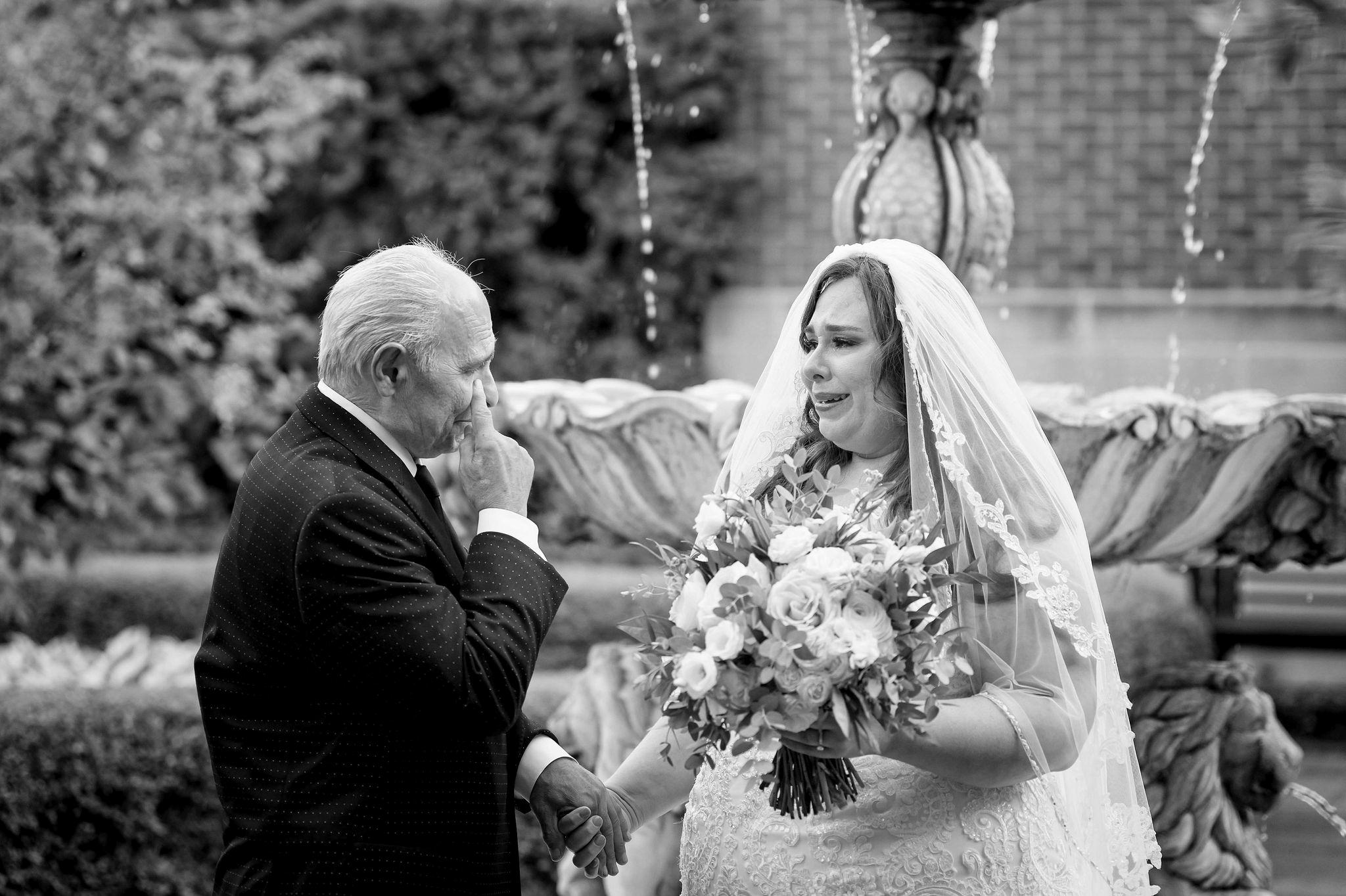 A dad wipes away a tear while his daughter, the bride, also cries after seeing each other for the first time on her wedding day.  