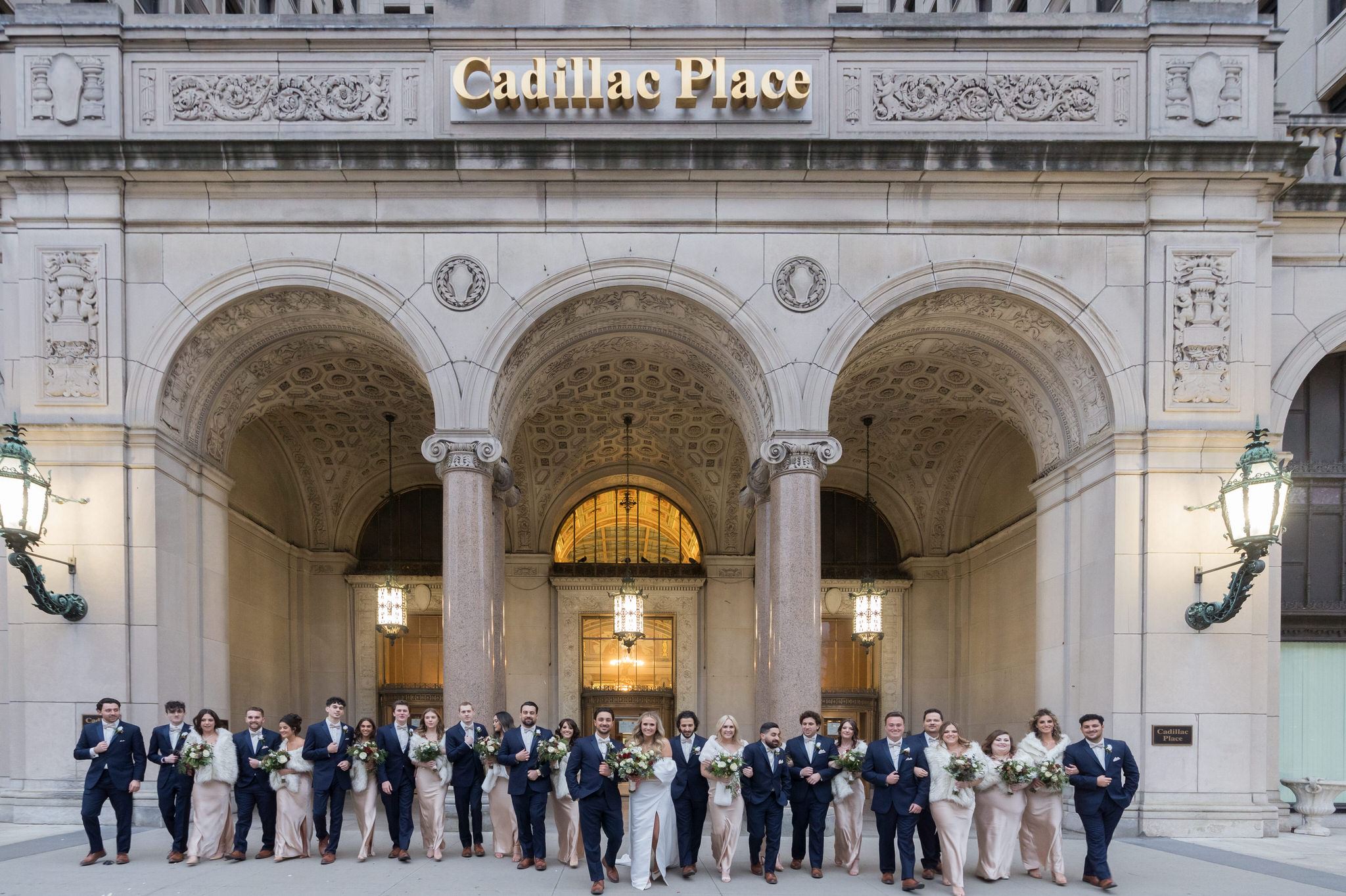 A large bridal party poses in front of Cadillac Place in Detroit, MI.