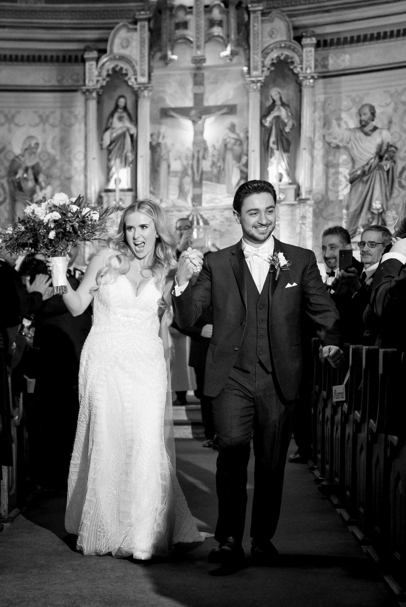 A bride and groom celebrate and smile as they walk down the aisle of Holy Family Catholic Church. 