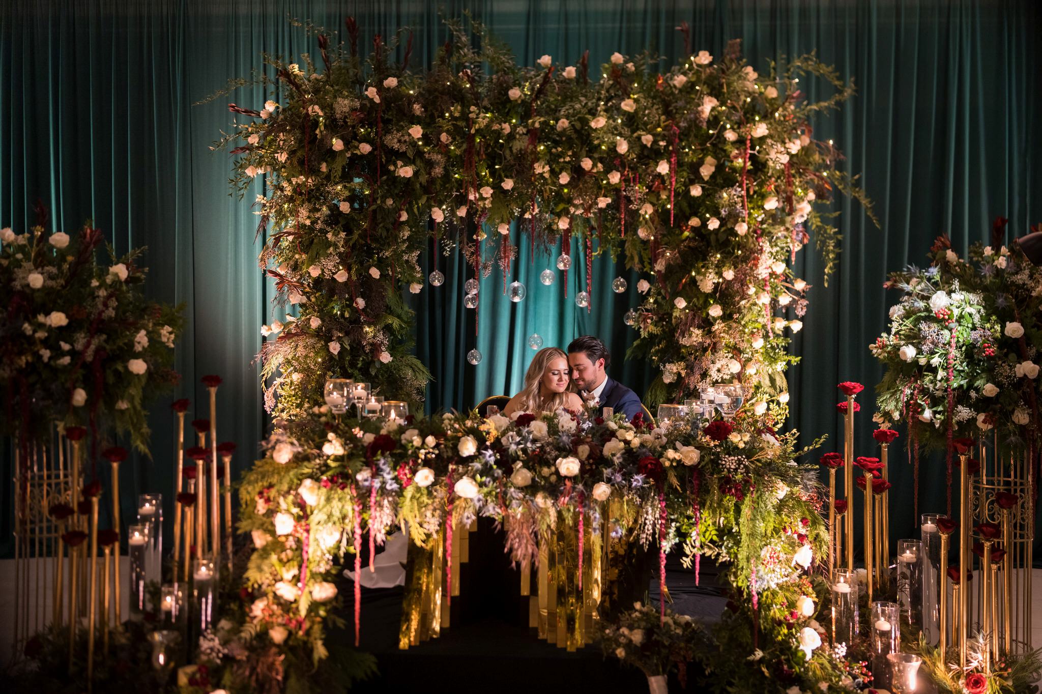 A couple poses seated amid floral arrangements at their Penna's of Sterling wedding reception.