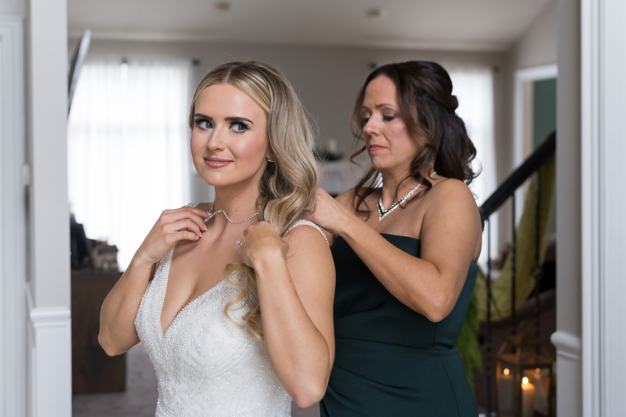 A bride gets help putting her necklace on from her mom on her wedding day.  