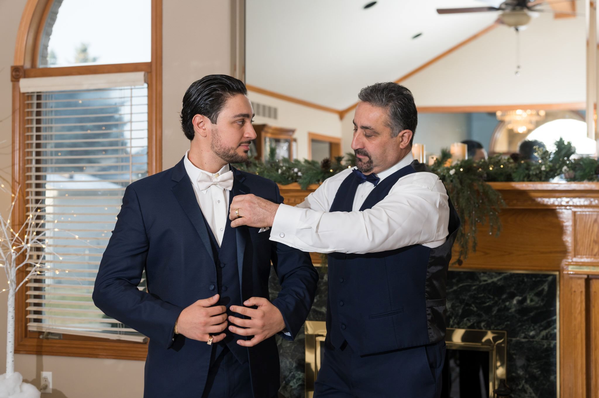 The groom receives help getting dressed from his dad on his wedding day.   