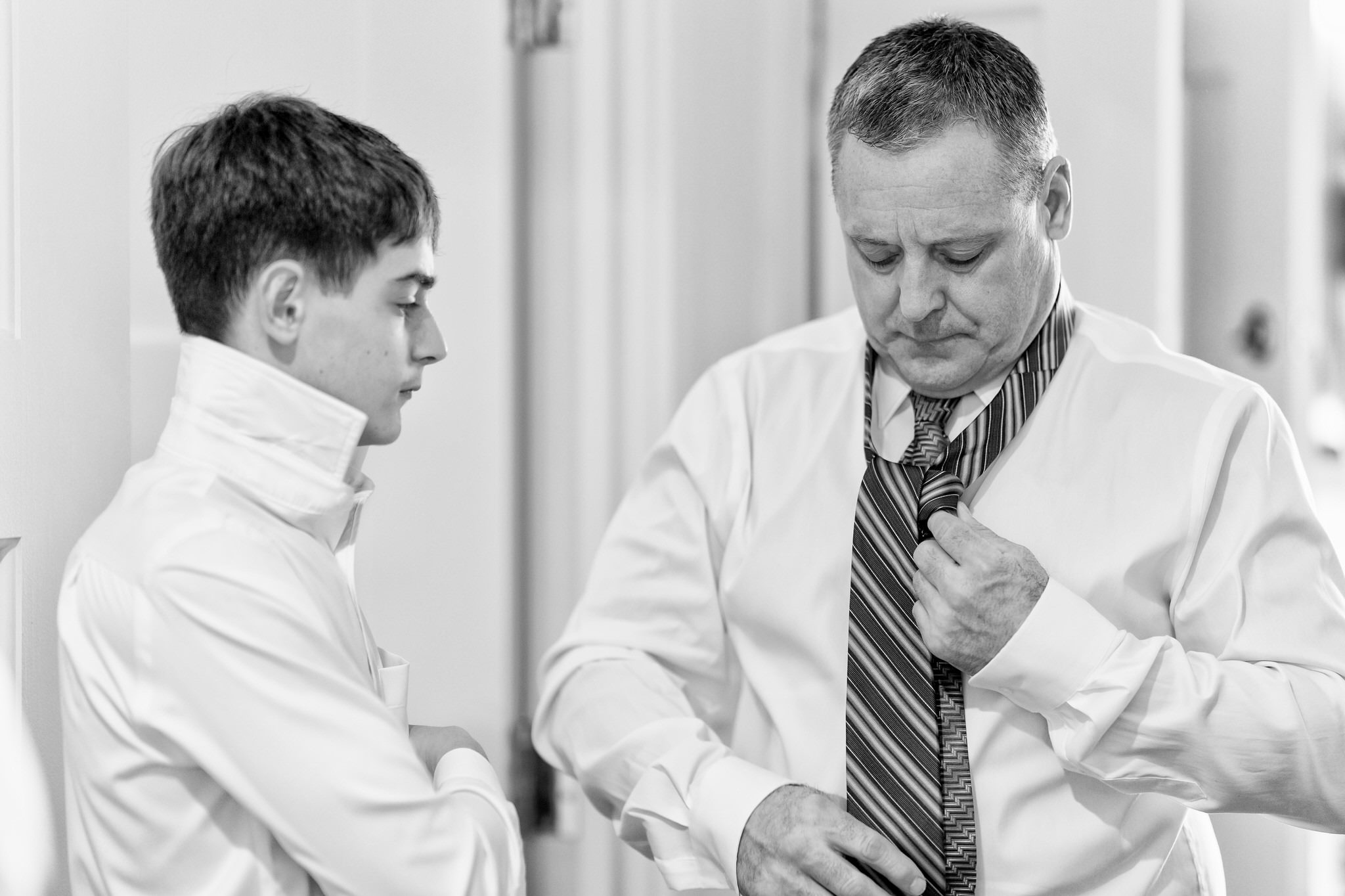 Black and white photo of a dad helping his son tie a tie.  