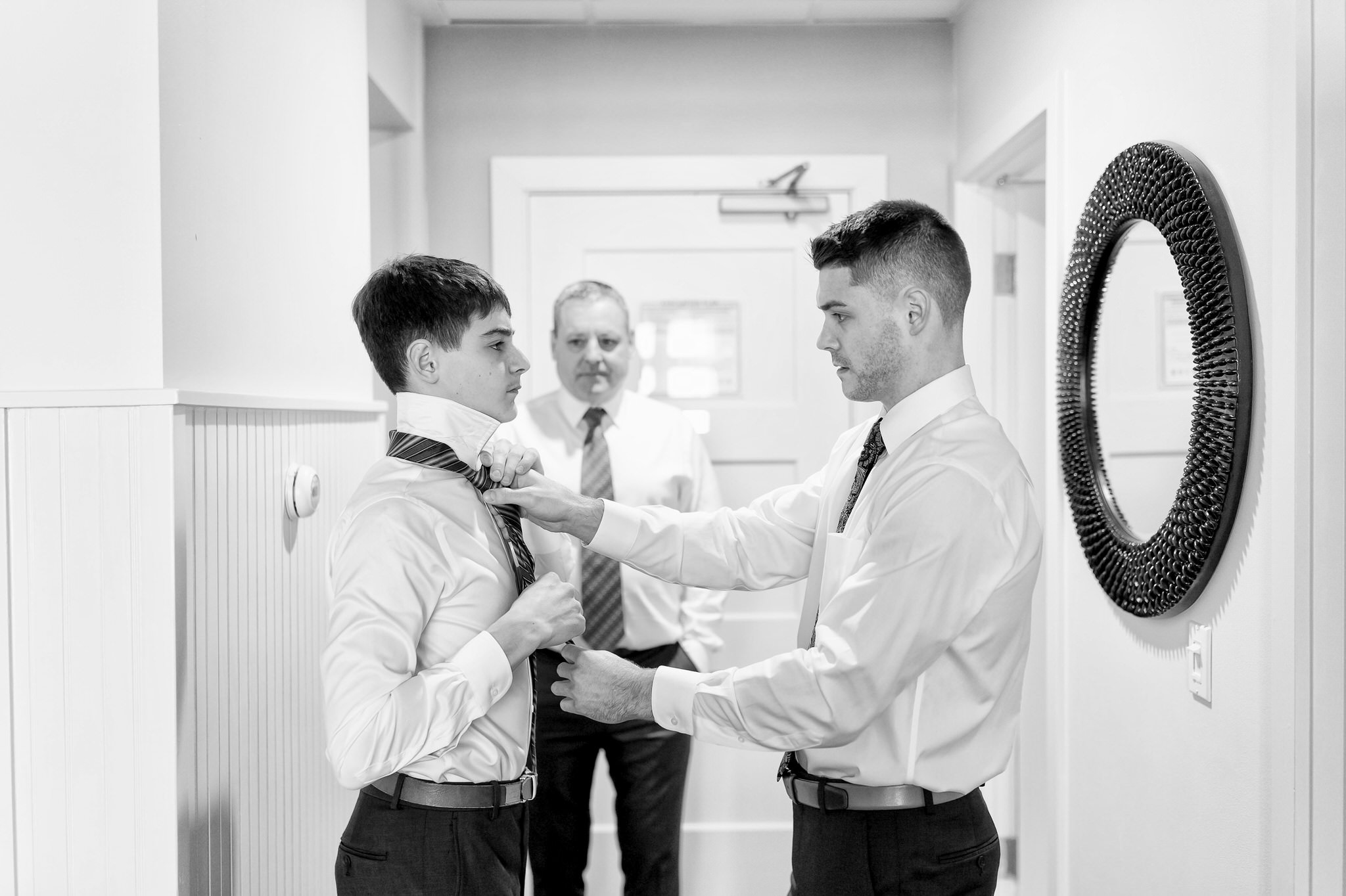 Older brother helping adjust his brother's tie while their dad watches.  