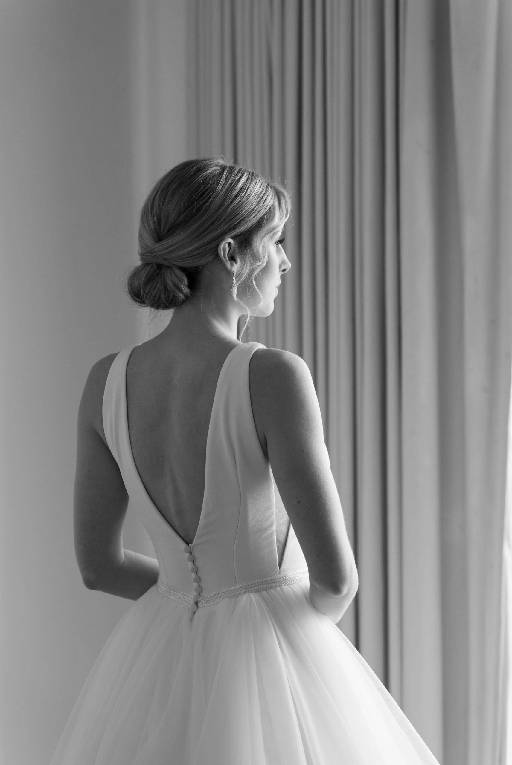 A black and white photo of the back of a bride and she looks outside before her Bay Harbor wedding. 