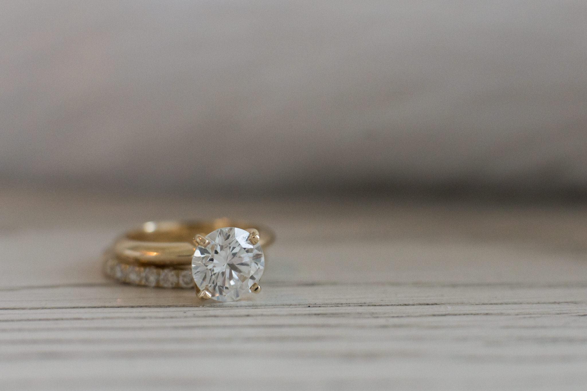 A diamond engagement ring sits on top of white wood.