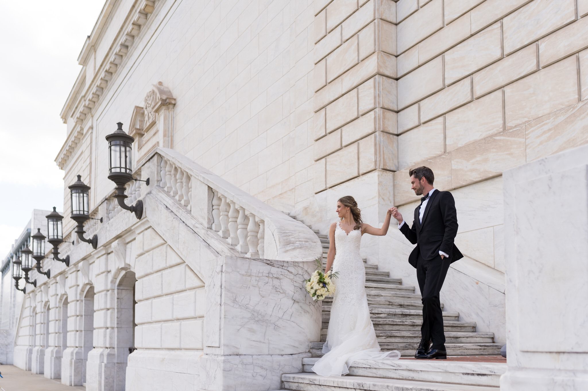 A bride and groom pose on the steps of the Detroit Institute of Art on their wedding day.  