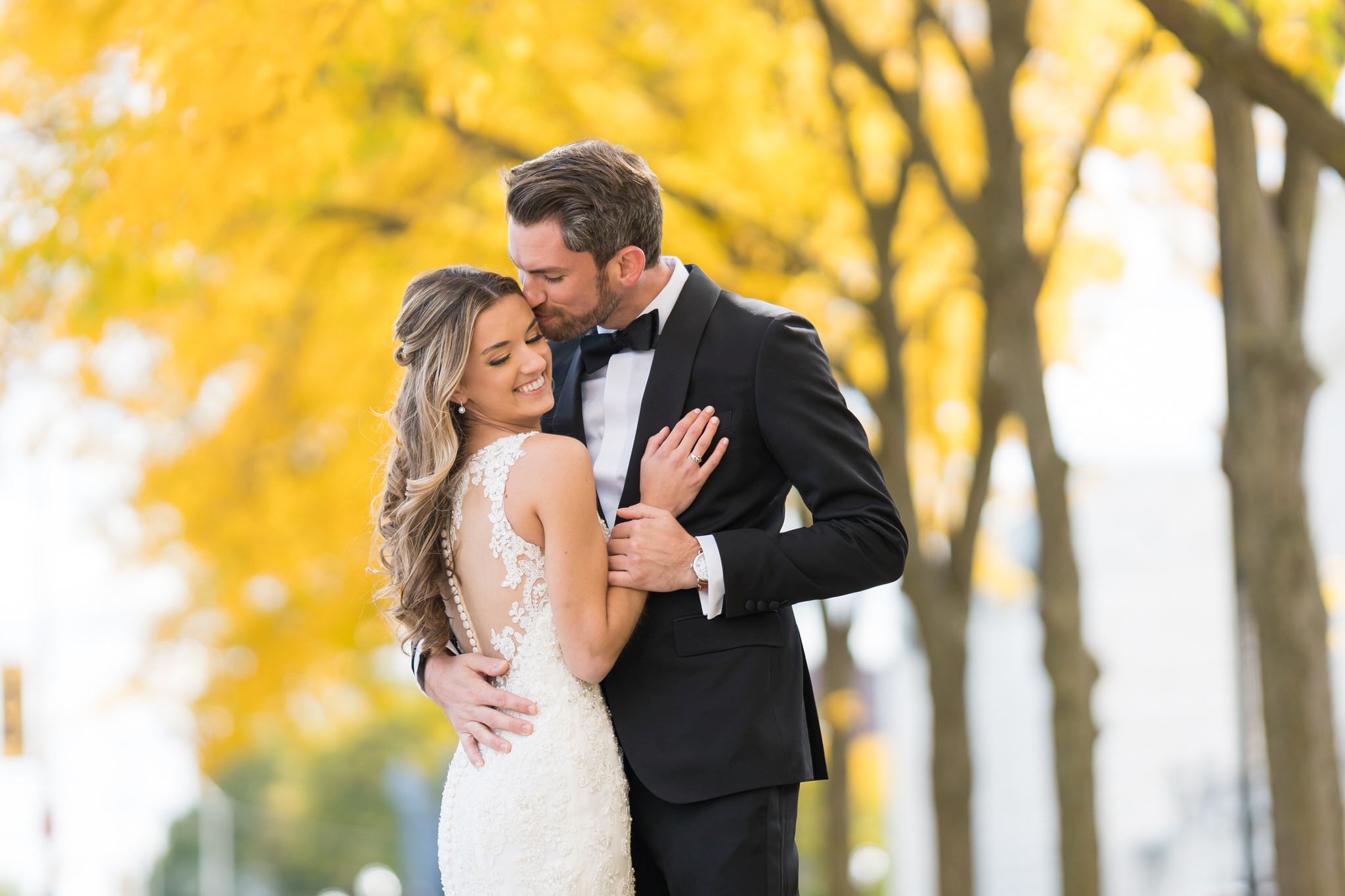 With her hand on his chest, a bride and groom pose with yellow trees in the background at the Detroit Institute of Art.