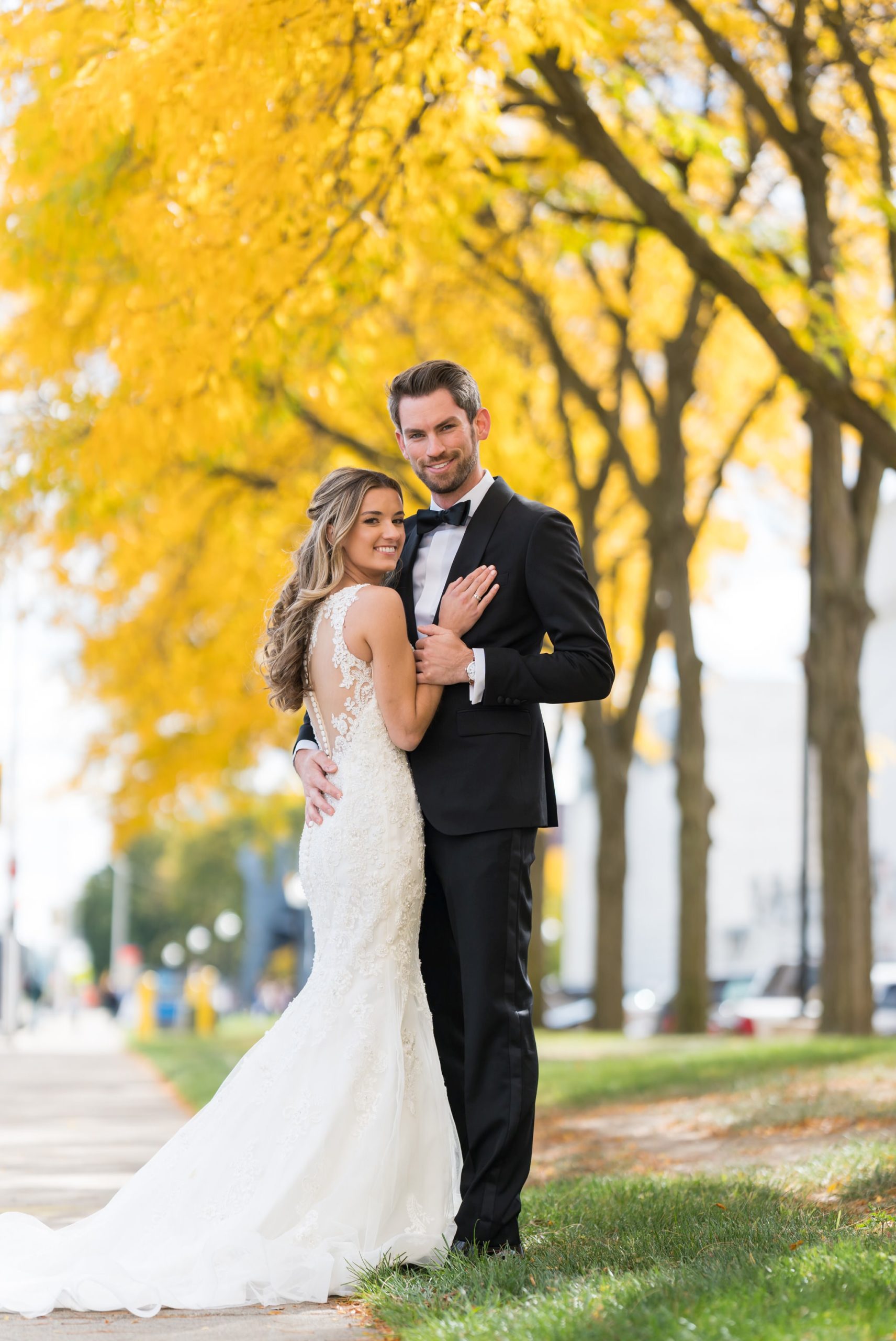 With her hand on his chest, a bride and groom pose with yellow trees in the background at the Detroit Institute of Art.