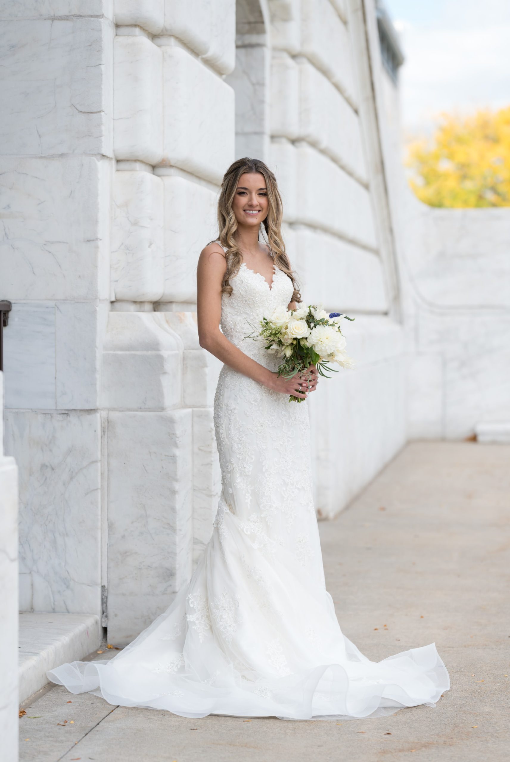 A bride, holding her bouquet, poses for a full length portrait outside of the Detroit Institute of Art on her wedding day.  