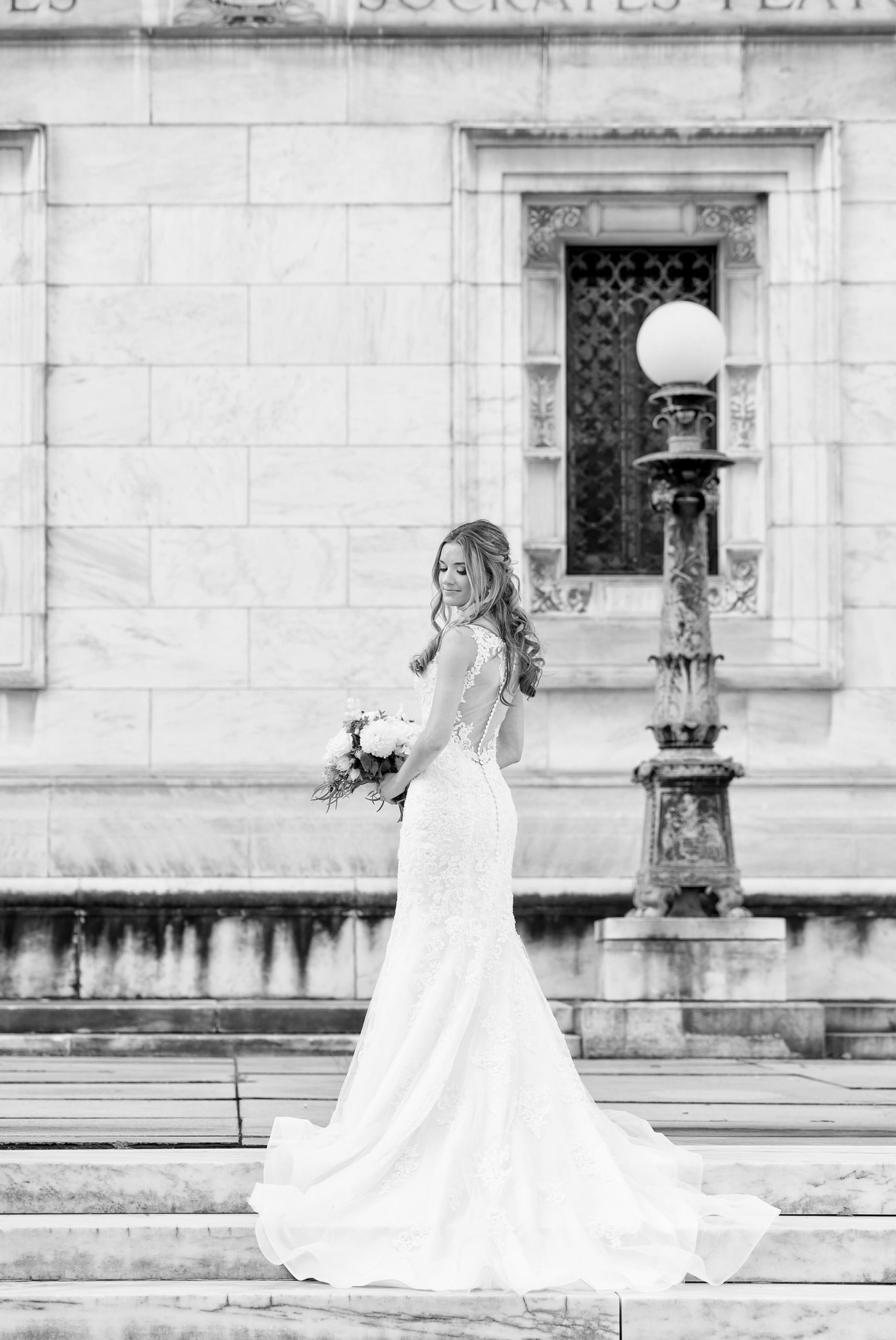 A bride poses, showing off the back of her dress, on the steps of the Detroit Public Library.