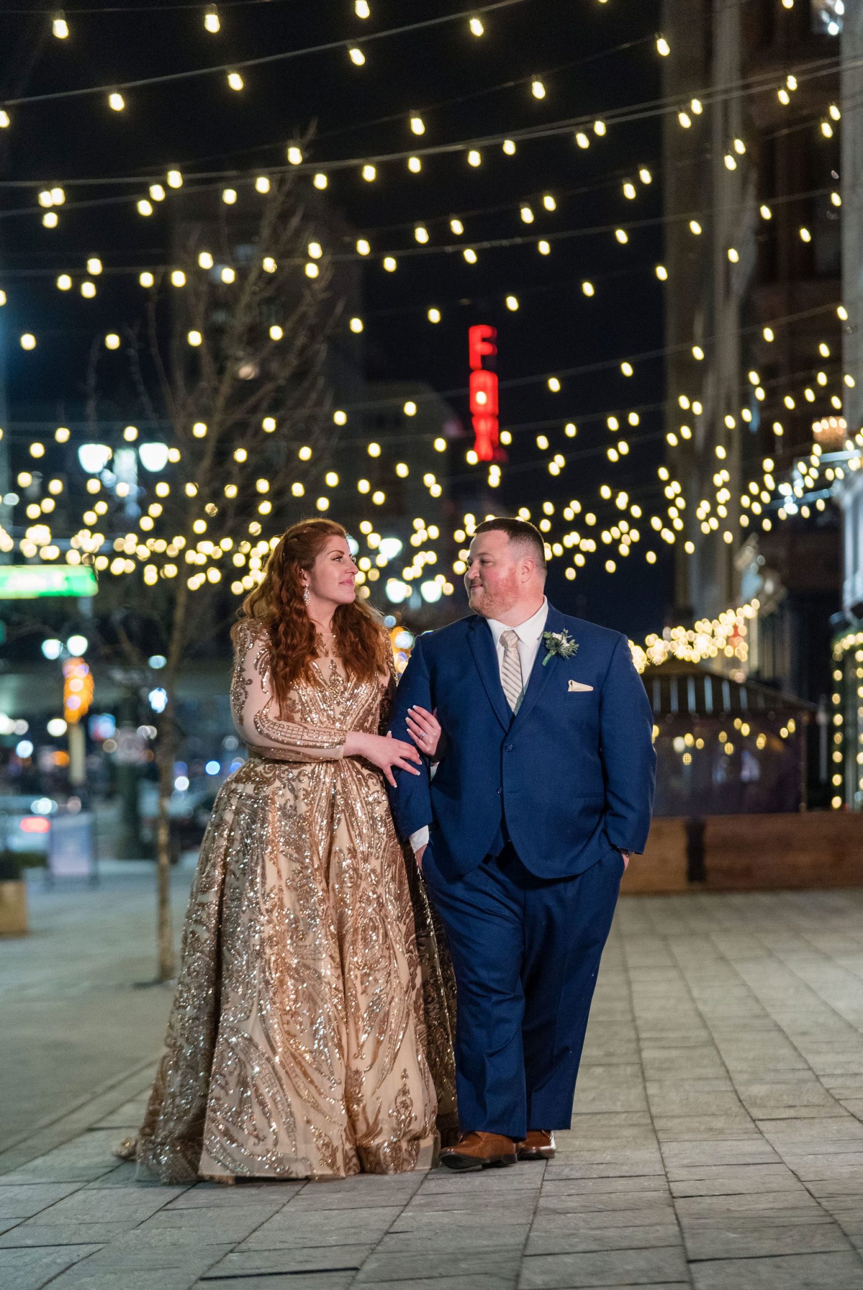 A couple, arms linked, walk along Woodward at night during their Detroit elopement. 