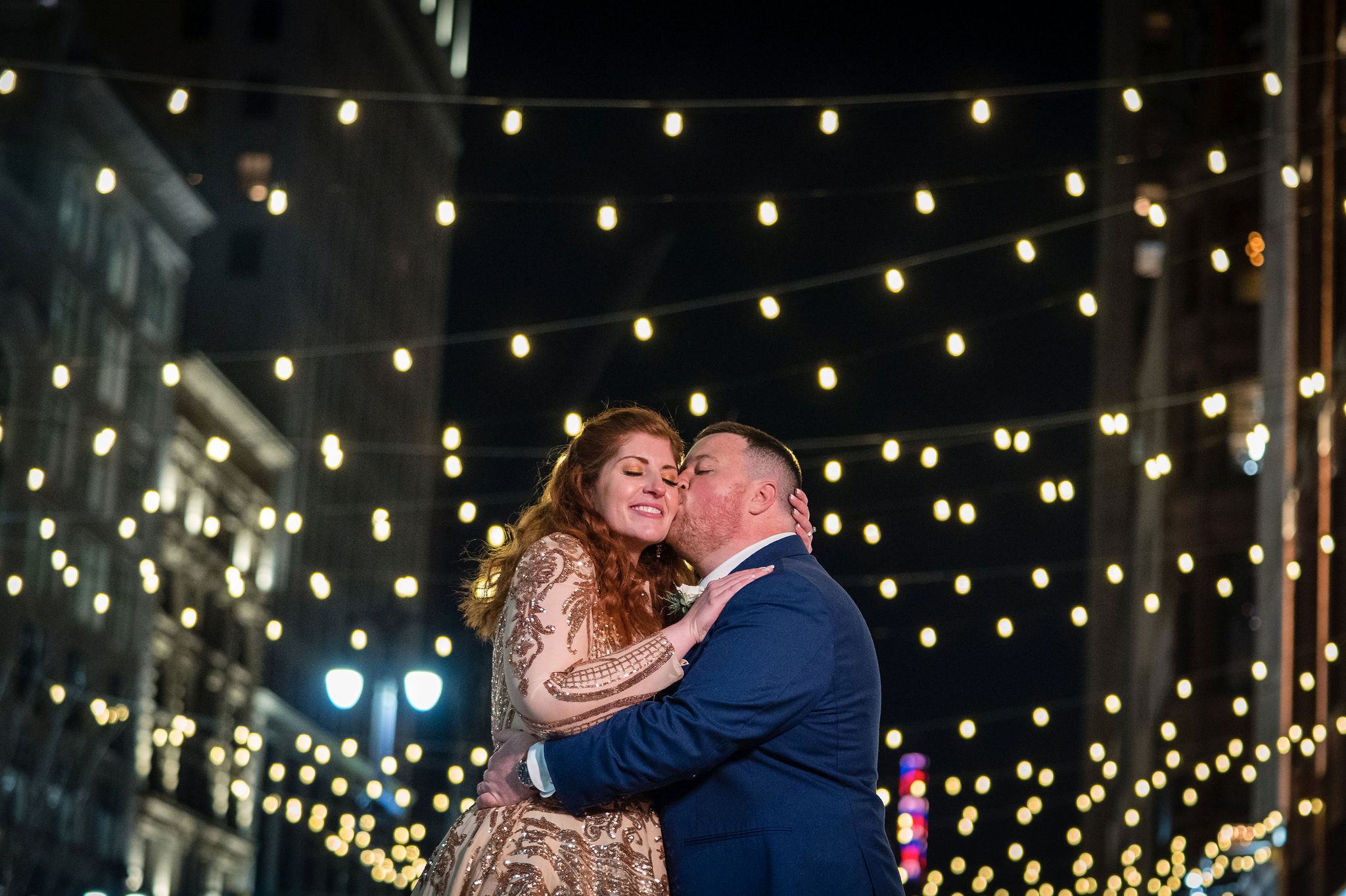 A couple embrace and kiss with twinkle lights in the background during their Detroit elopement. 