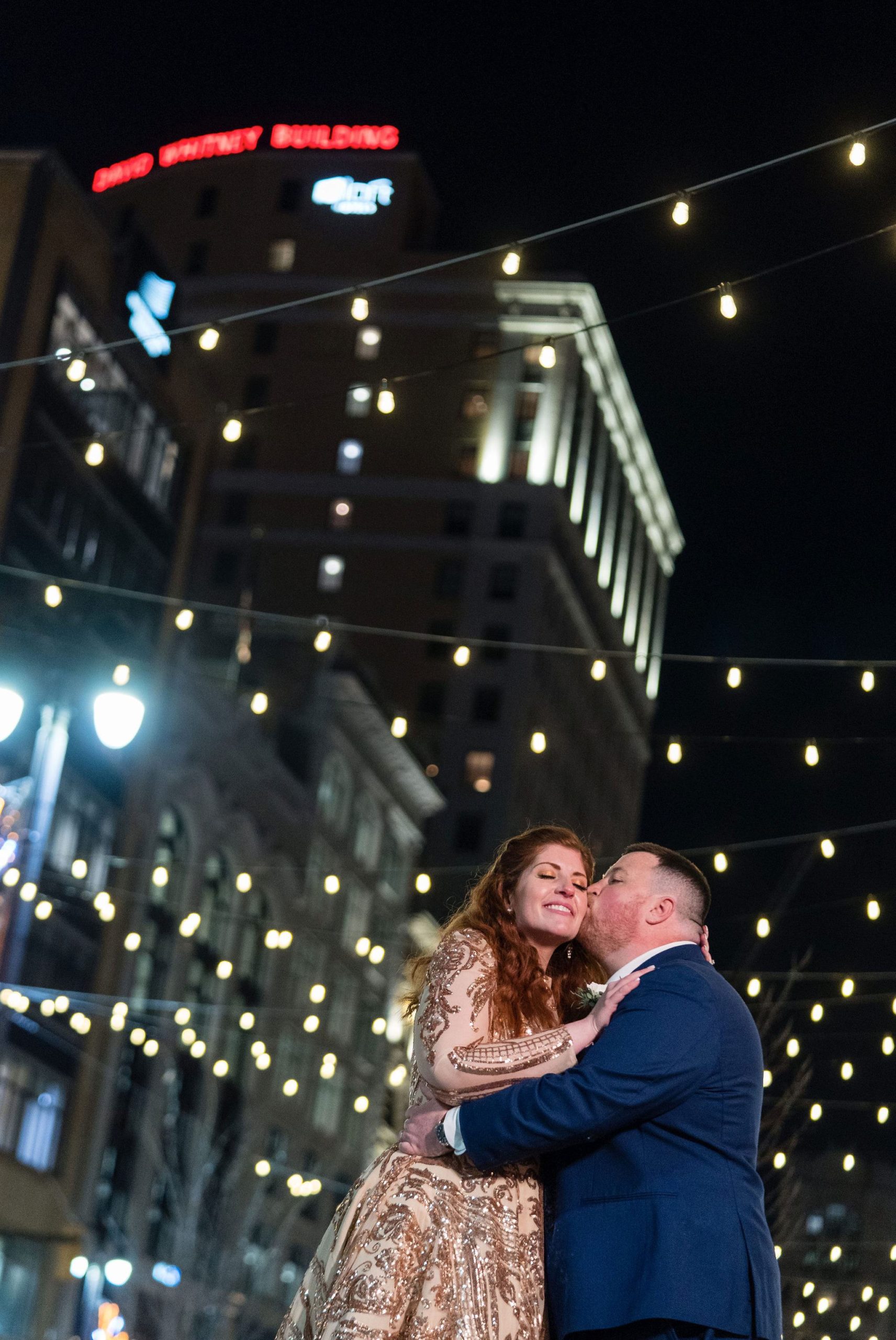 A couple embrace and kiss with twinkle lights in the background during their Detroit elopement. 