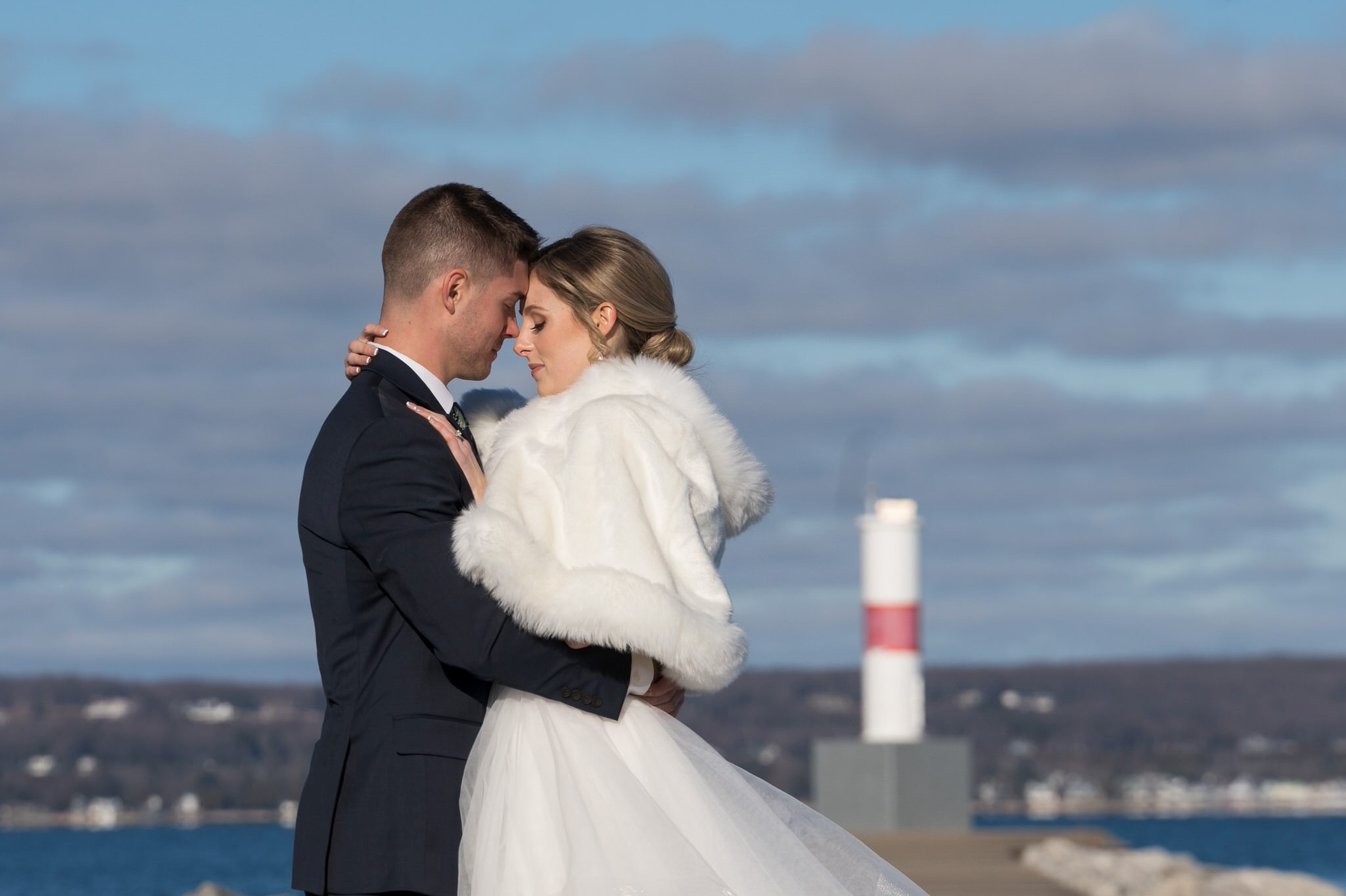 A bride and groom nuzzle near the Petoskey Pierhead Lighthouse before their Bay Harbor wedding ceremony.  