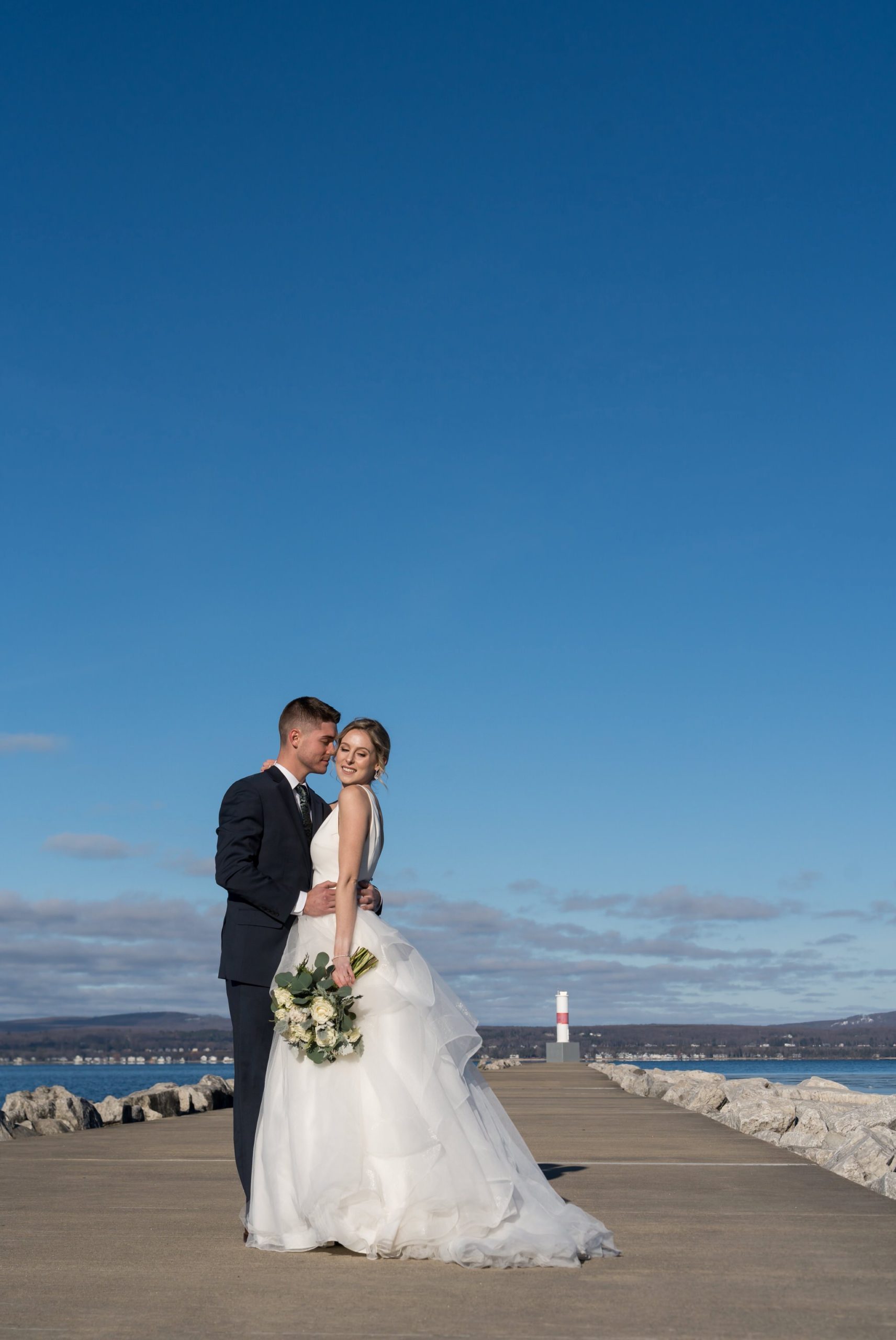 A bride and groom embrace near the Petoskey Pierhead Lighthouse before their Bay Harbor wedding ceremony.  