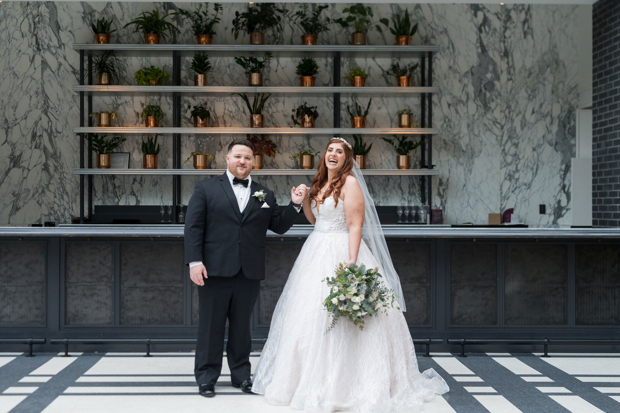 A bride and groom hold hands and laugh during their first look at their Shinola Hotel wedding.  