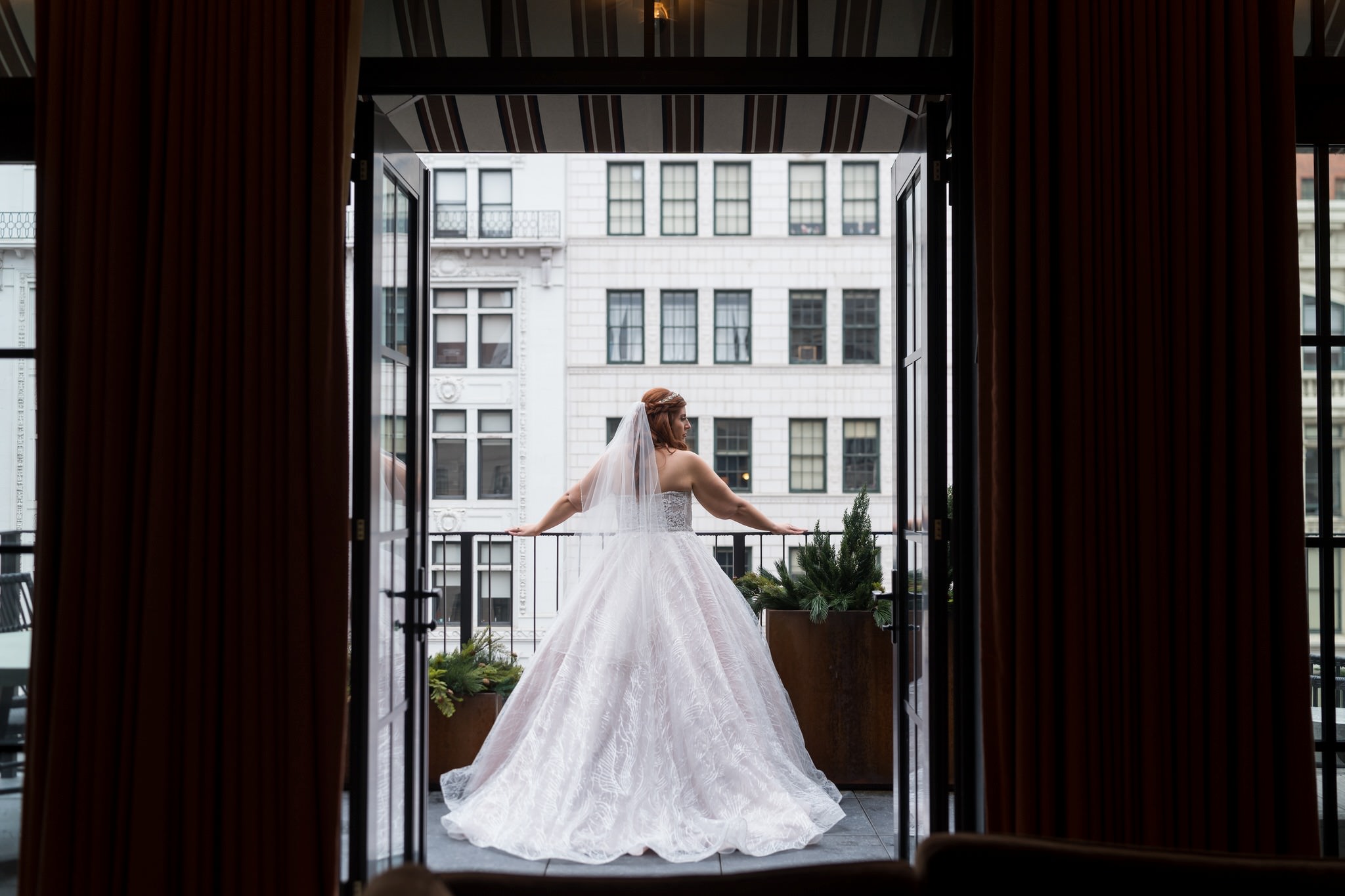 A bride is framed in a doorway, standing on a balcony overlooking Detroit, on her Shinola Hotel wedding day.  