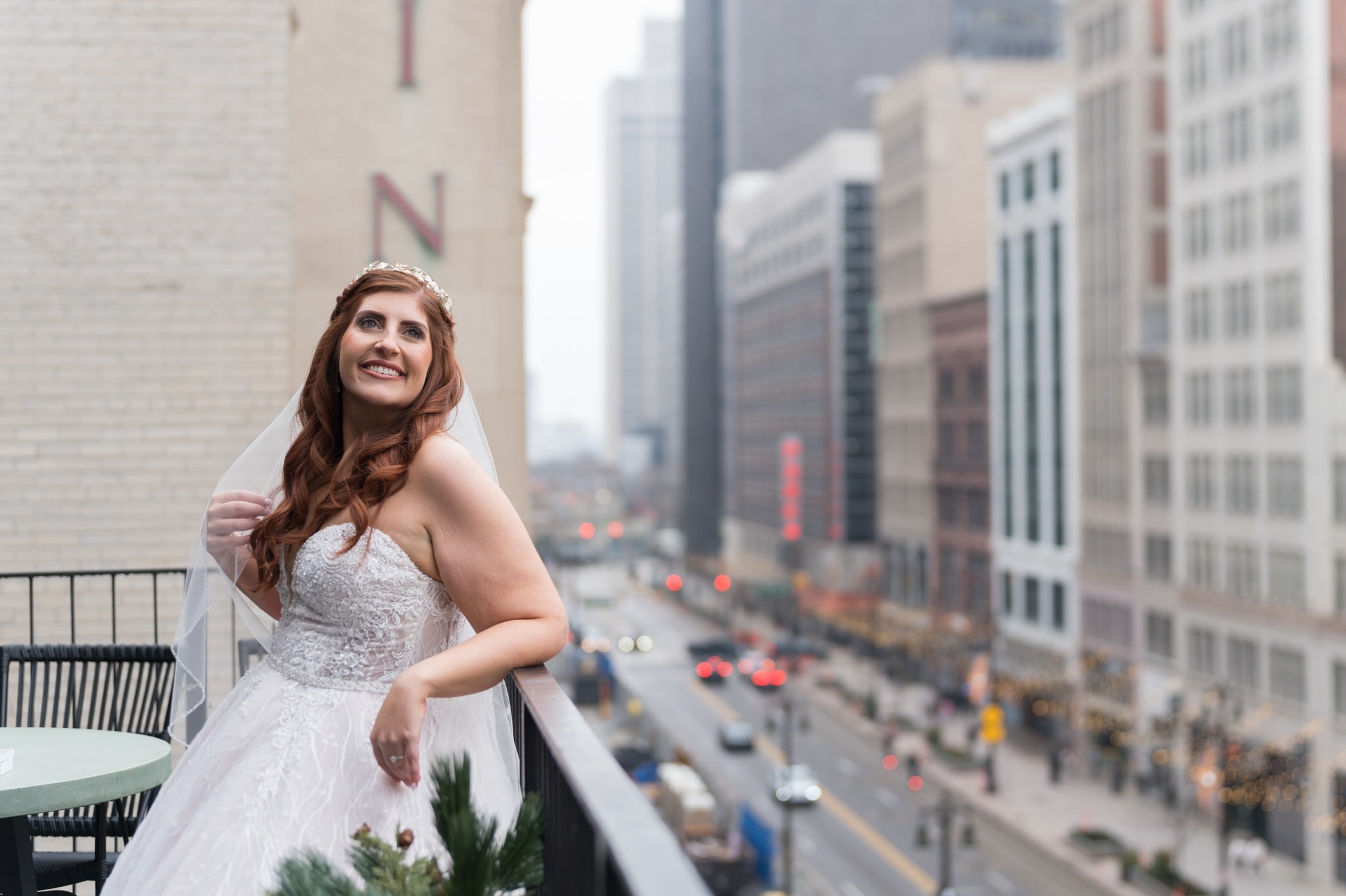 A bride causally leans against a railing looking down Woodward in Detroit on her Shinola Hotel wedding day. 