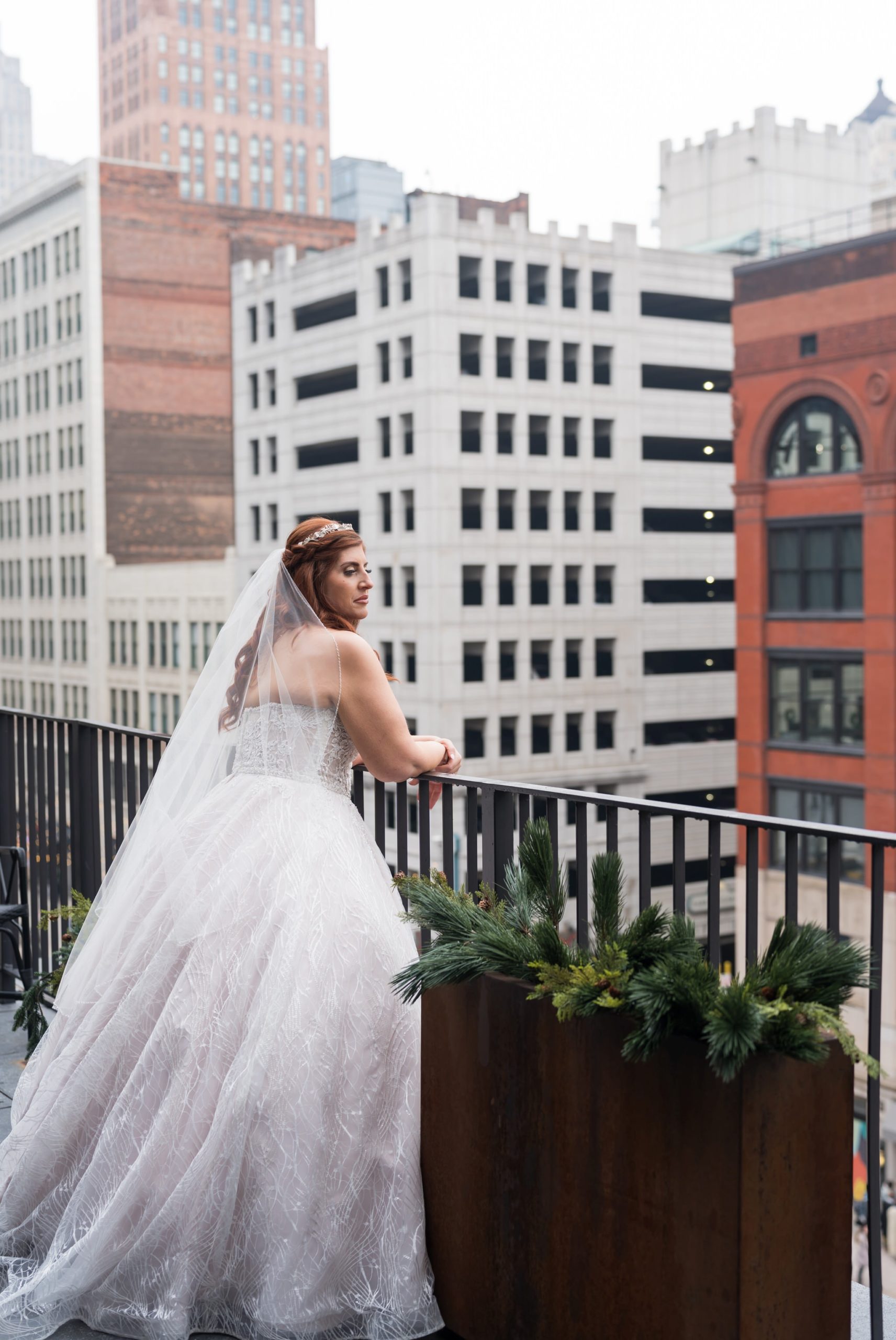 A bride causally leans against a railing looking down Woodward in Detroit on her Shinola Hotel wedding day. 