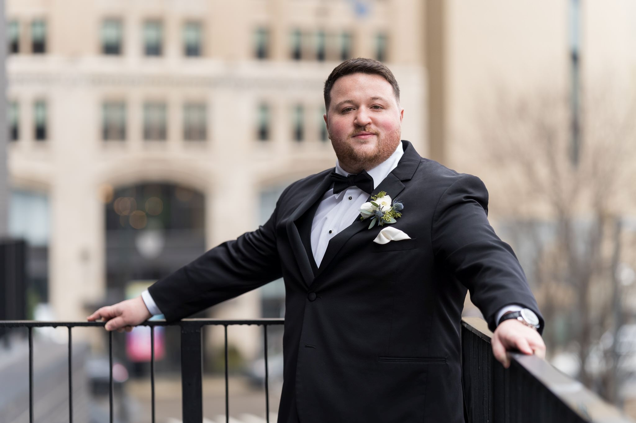 A groom causally leans against a railing looking down Woodward in Detroit on her Shinola Hotel wedding day. 