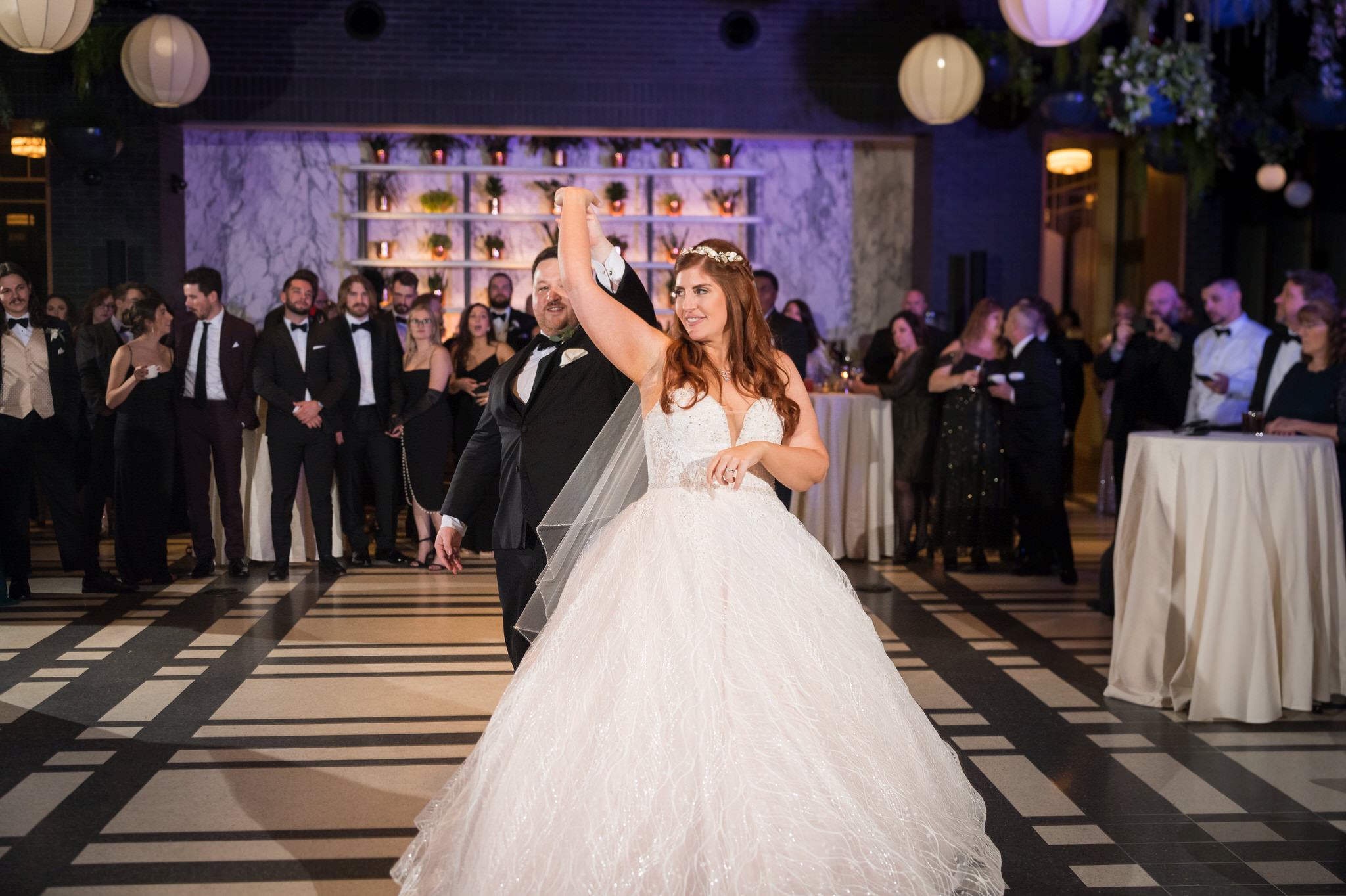 Accented with purple uplighting, a bride and groom share a first dance at their Shinola Hotel wedding reception.