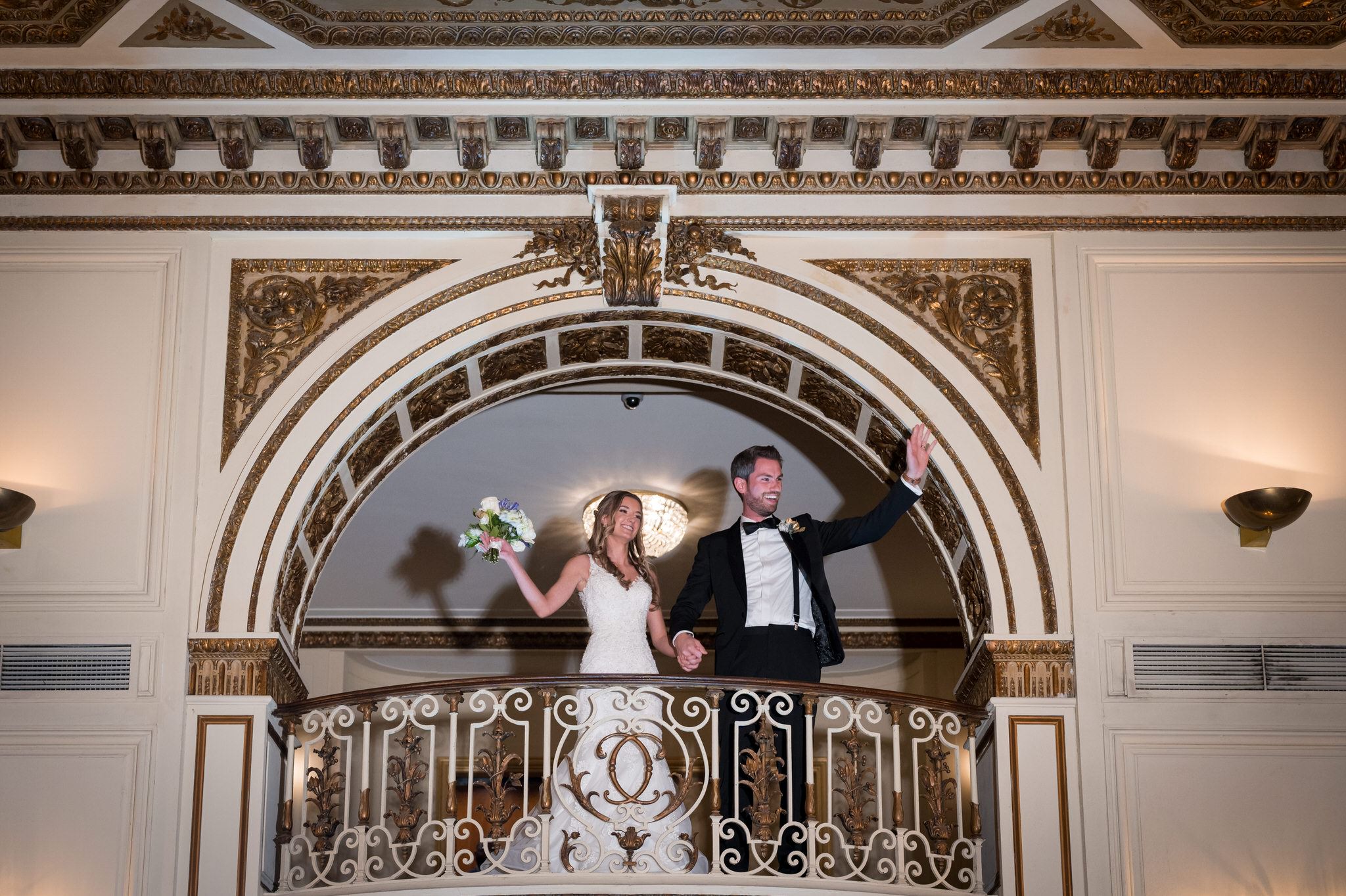 A bride and groom wave to their guests from the balcony of their wedding at Detroit's Colony Club. 