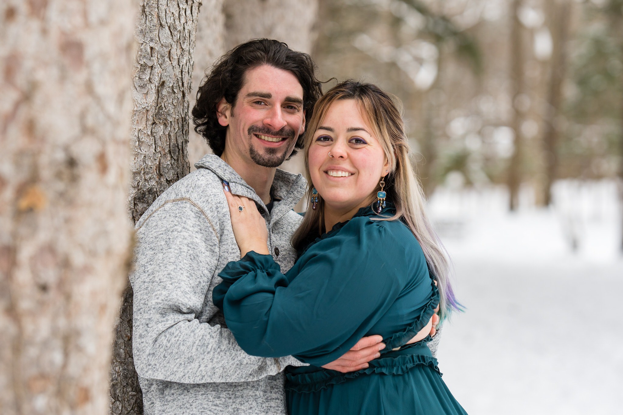 A couple pose with a tree in the snow for their winter engagement session at Stony Creek. 