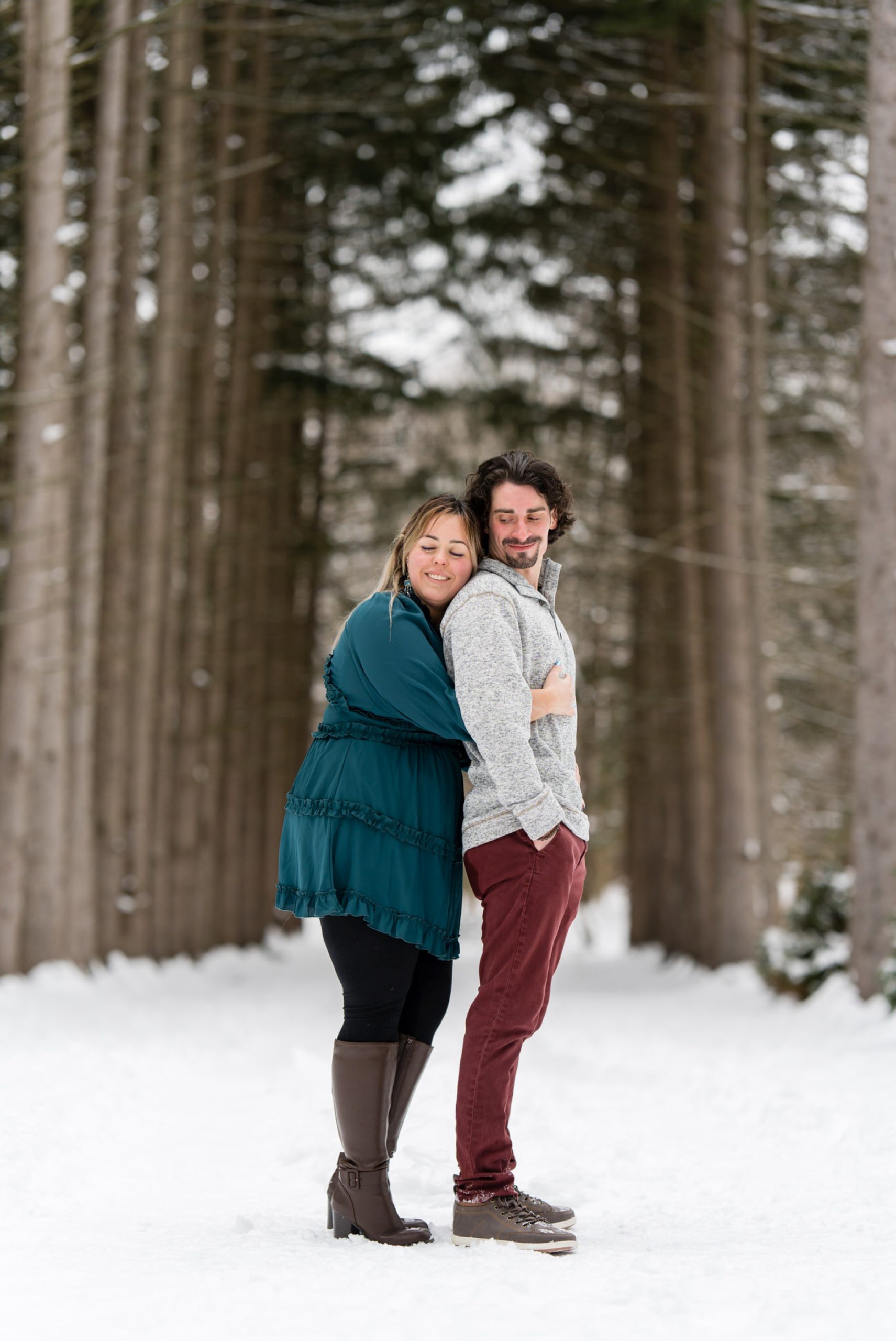 A woman hugs her boyfriend from behind in a tunnel of trees at their winter engagement session at Stony Creek. 