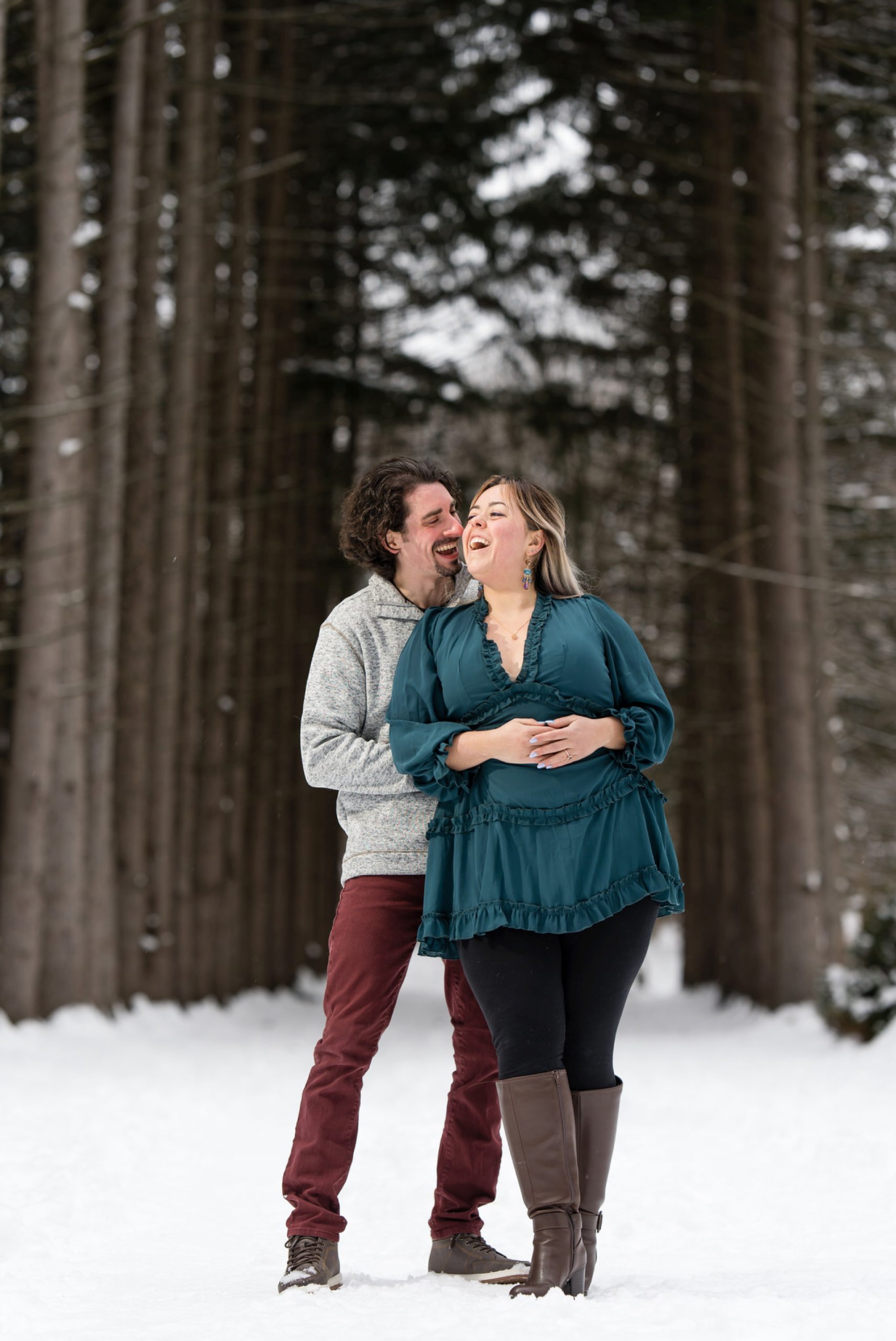 A guy hugs his fiance from behind while they both laugh at their winter engagement session at Stony Creek Metropark.